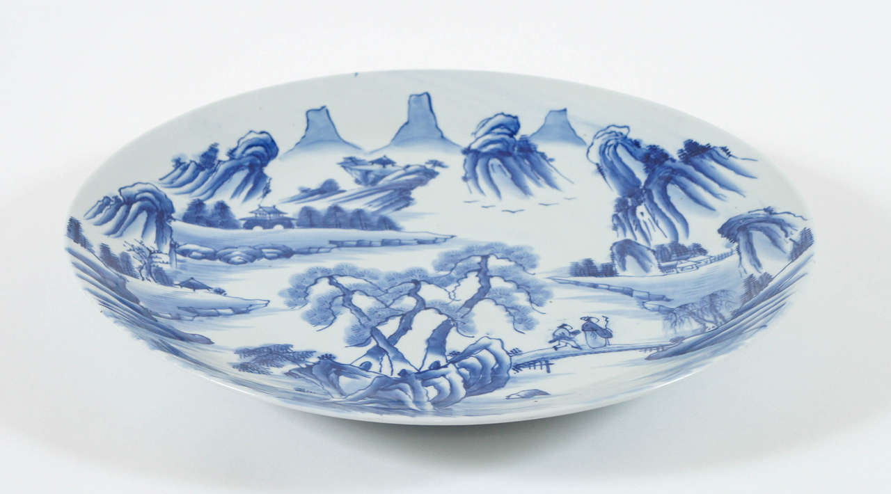 Japanese circa 1880 Meiji period Arita blue and white porcelain charger of large size having all-over underglaze painted chinoiserie mountain landscape design with two figures crossing a bridge.