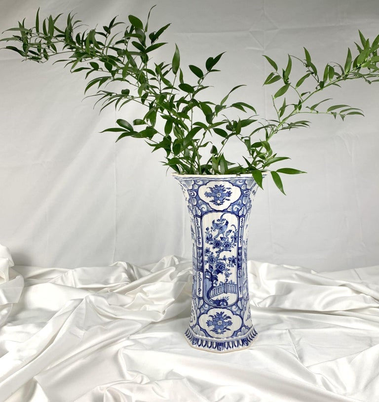 This large Delft vase is painted in tones of blue and white.
 We see four alternating panels.
Two panels show a songbird in the garden of a flowering fruit tree.
The other two panels show a man on a bridge calling up to his lover in the window of
