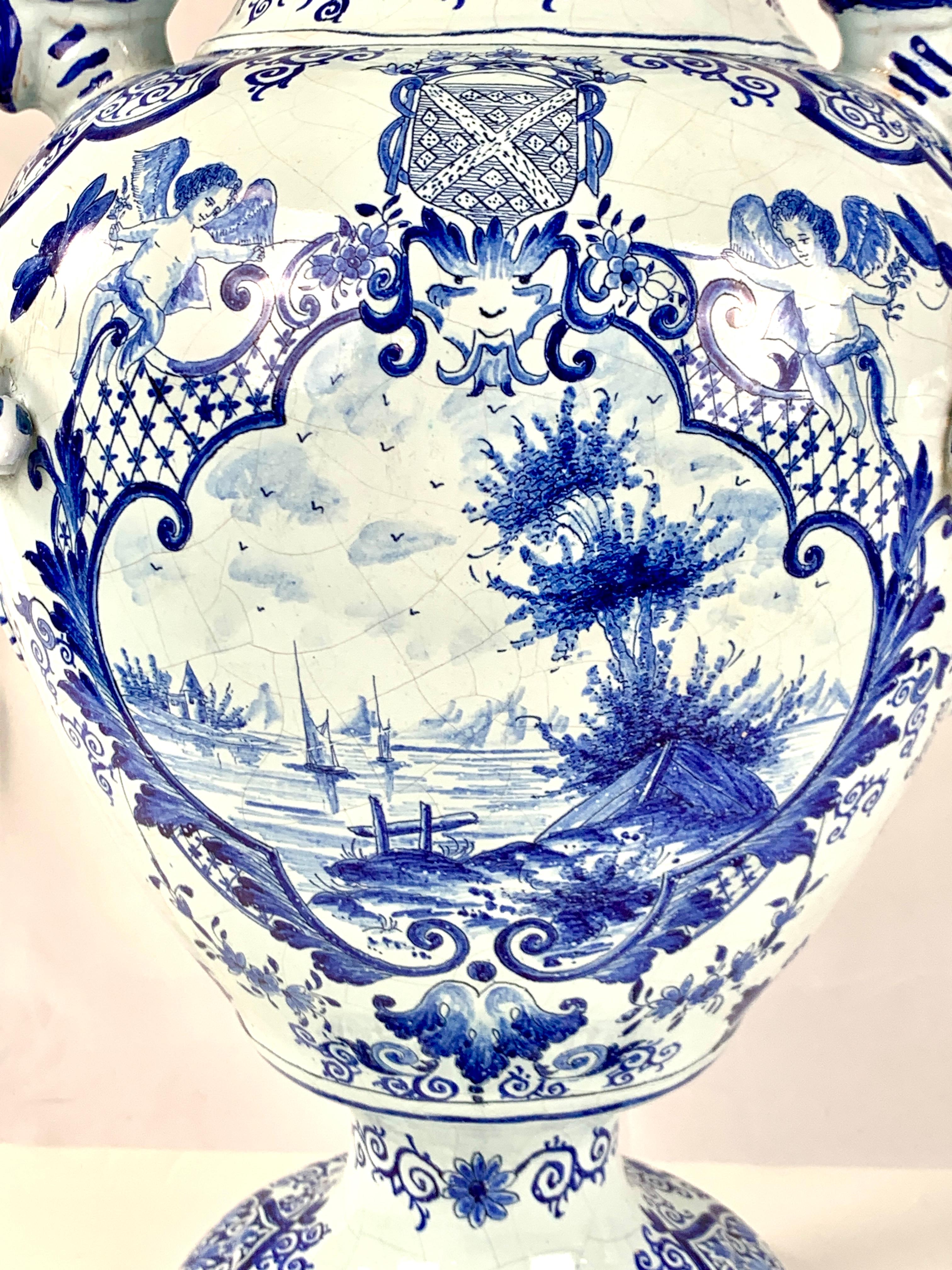 The first thing you notice is the magnificent spiral snake handles. 
This large blue and white Dutch Delft covered jar is fully decorated!
The elaborate decoration on the front features a lovely waterside scene topped with an armorial shield