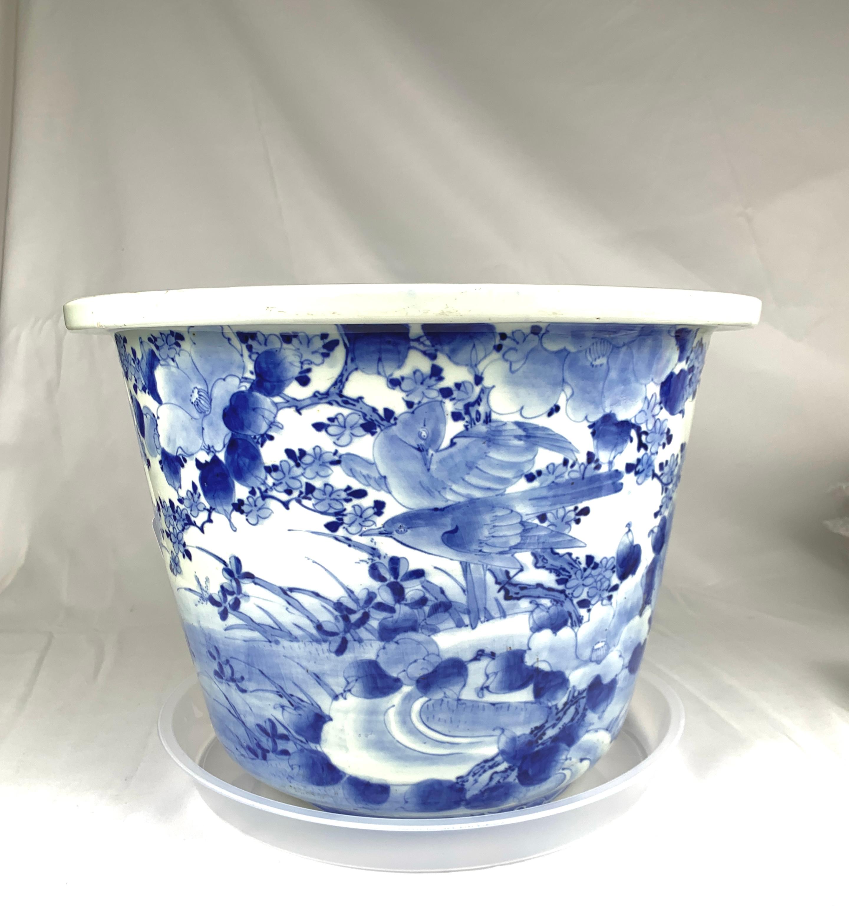 Dieses große, blau-weiß dekorierte japanische Porzellangefäß aus dem frühen 20. Jahrhundert steht auf drei Stummelfüßen (siehe Abbildungen).
Die Kanne ist mit einer traditionellen Szene aus blühenden Pflaumenbäumen, Singvögeln und einem sich