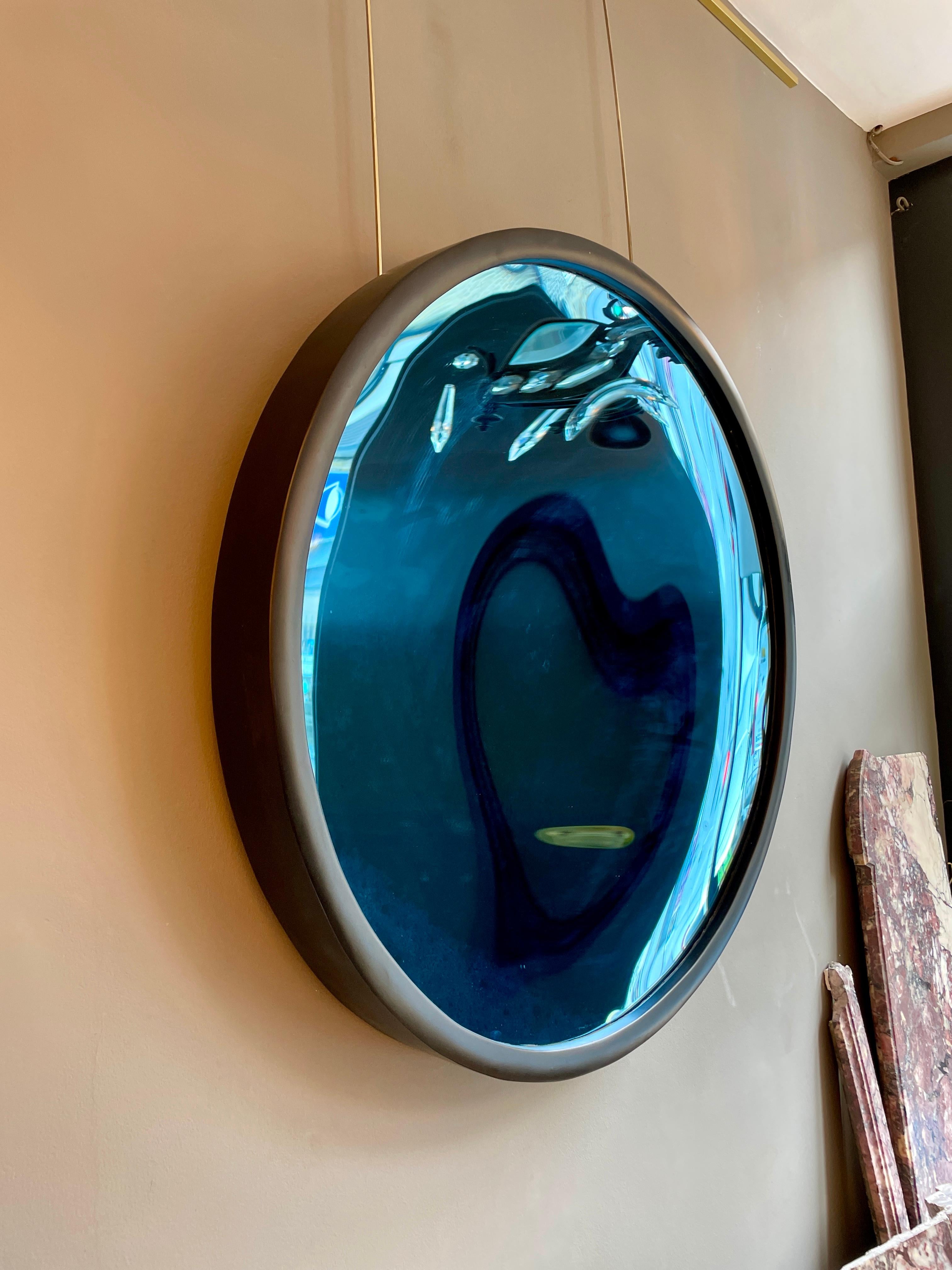 Grand miroir concave en verre bleu cobalt dans un cadre épais en bois ébonisé.