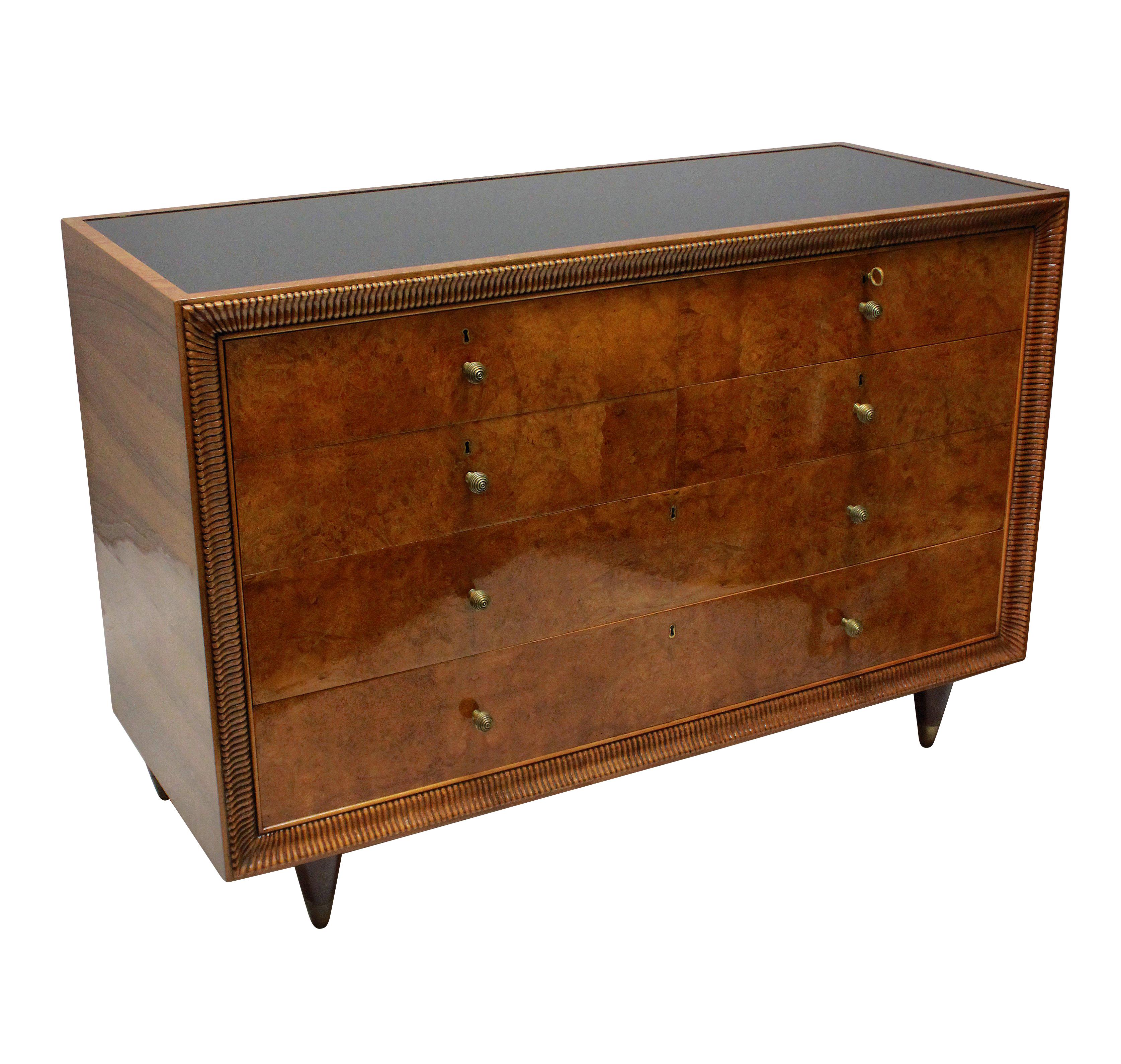 A large Italian commode of exceptional quality by Osvaldo Borsani. In lacquered bur walnut, with brass beehive handles, six lockable drawers and its original black glass inset top. The deeply carved frieze around the front of the piece is typical of