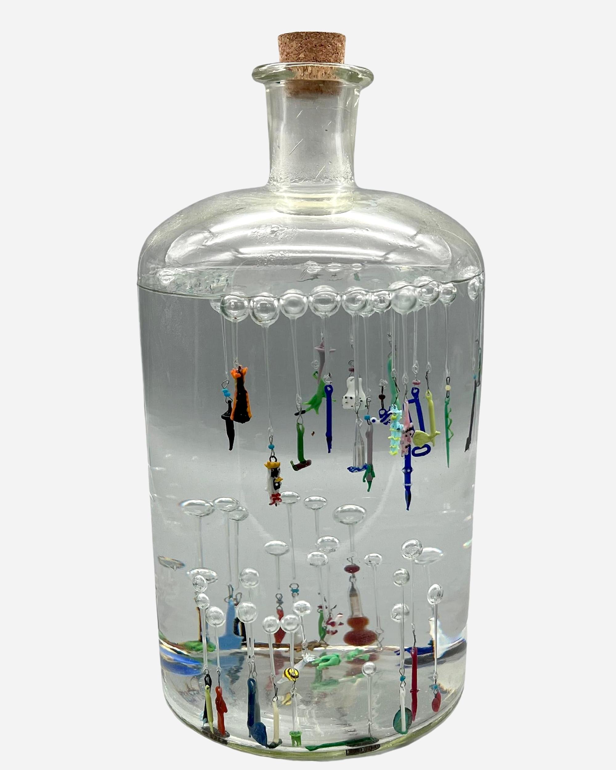 Numerous ludions float in a large, stoppered bottle of water. These are small figures or instruments in spun glass of various colors, attached to a bubble of transparent blown glass, floating on the surface of the water.The bottle, which closely