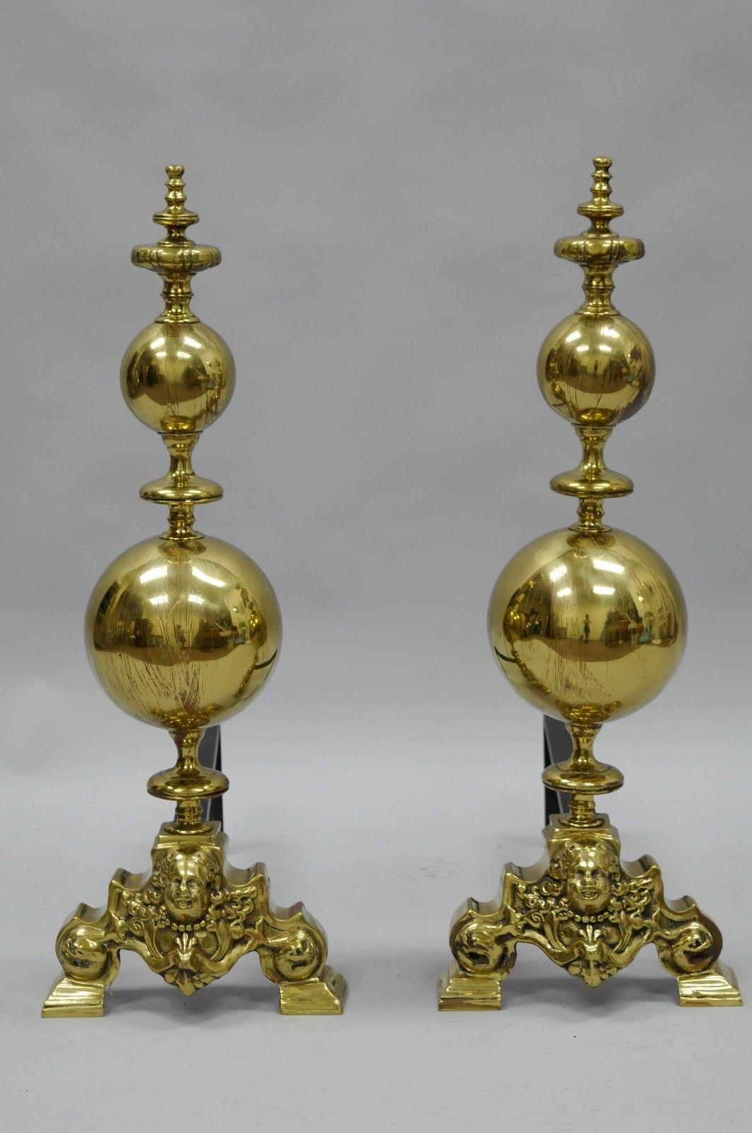 Impressive pair of antique brass large cannonball figural andirons in the French Empire style. Item features heavy brass forms, large round cannonballs, figural cherub faces, cast iron support, and brass finials, circa early to mid-20th century.