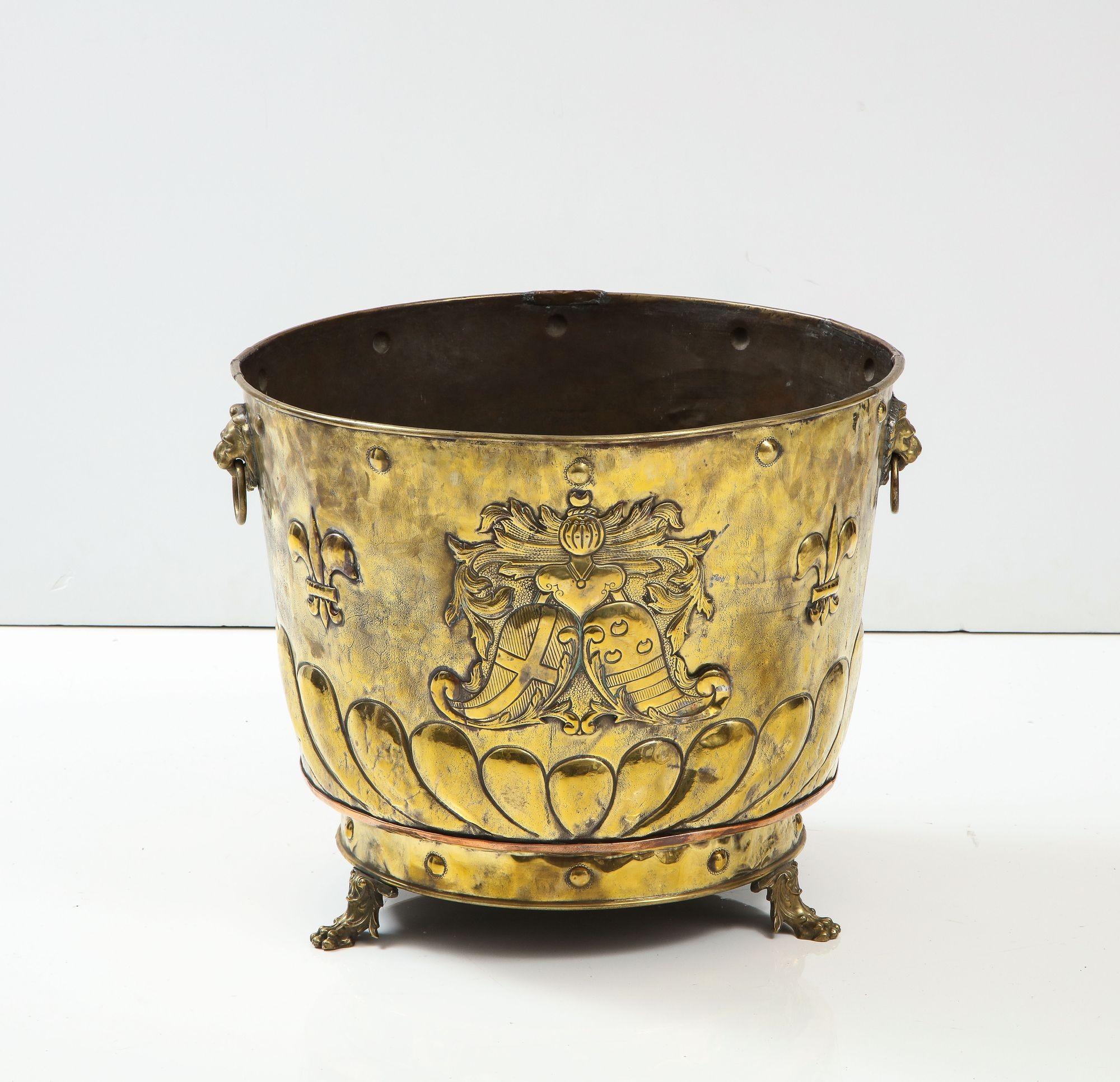 A large brass cauldron with repousee coat of arms, flower display and fleur-de-lys above button decorated lower rim with elaborately cast paw feet, having rolled top rim lion head mask handle rings to sides. A stunning piece of brass work, and