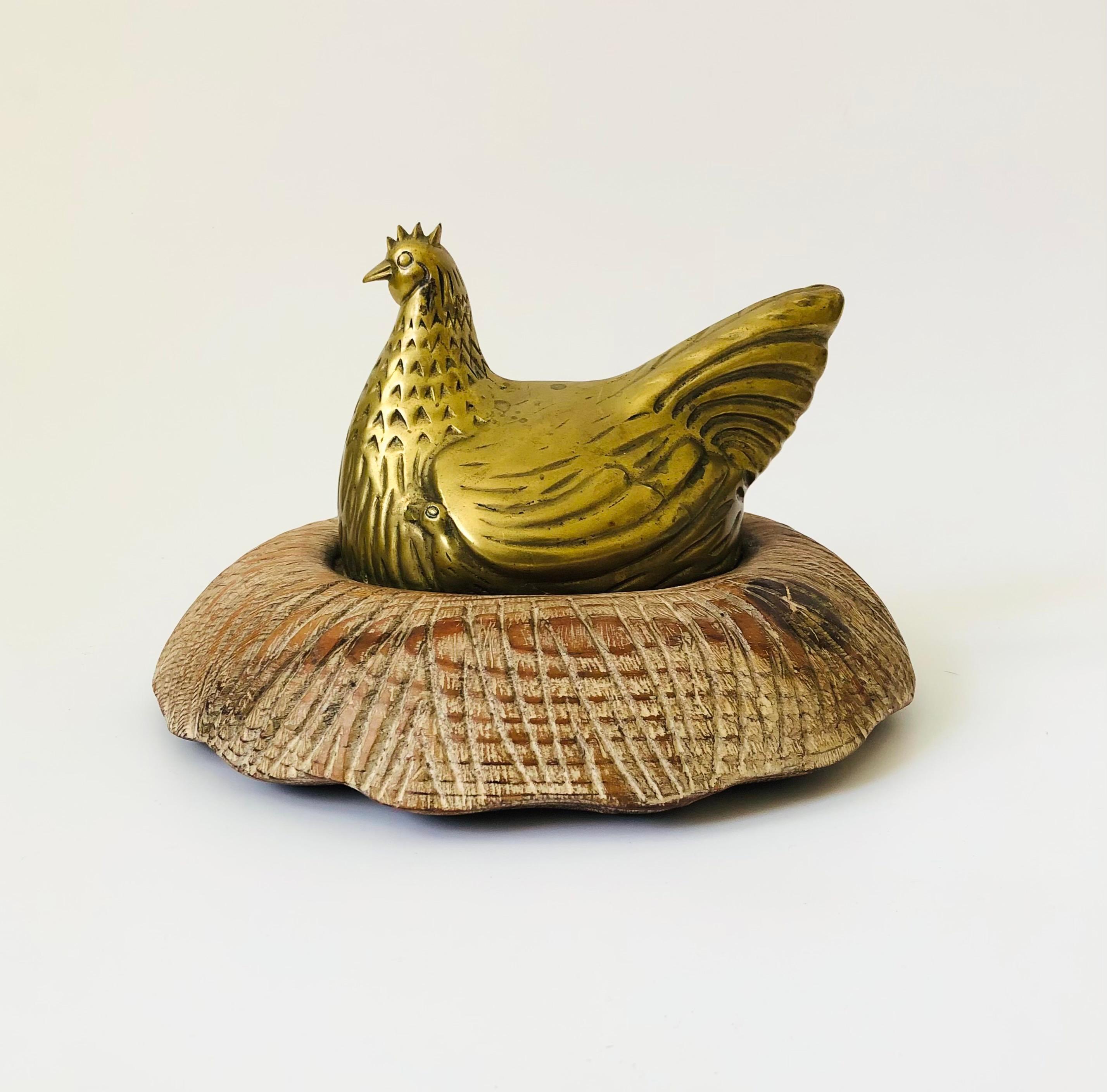 A large vintage brass chicken sitting in a carved wood nest. Great detailing formed into the brass with a distressed white washed finish to the wood nest. The original tag is no longer attached, however this is most likely a piece by Sarried Ltd.