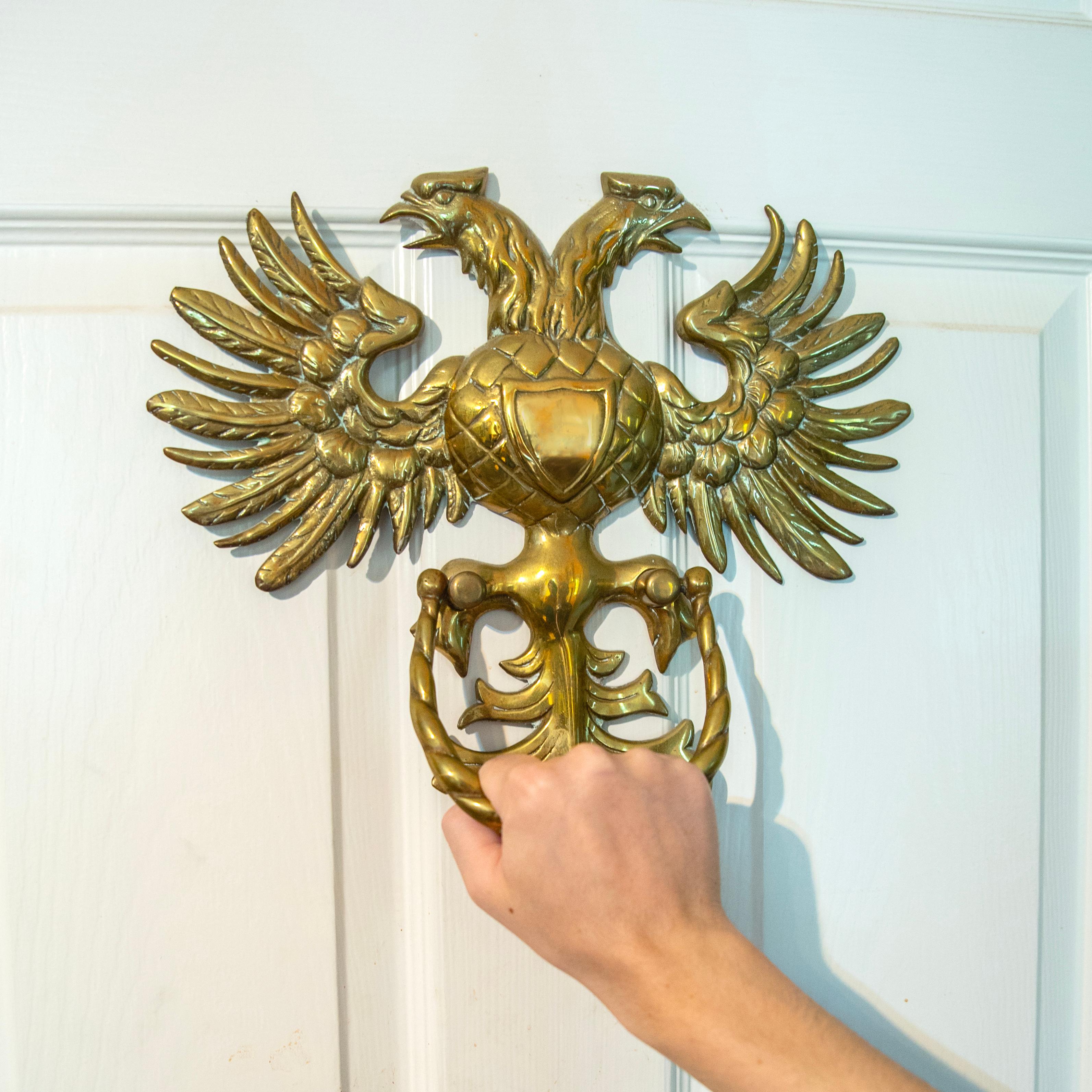 Designed as a stylized repoussé double headed eagle fashioned entirely of brass, detailing textured feathers, the wings and tail dramatically splayed, enclosing a polished blank shield, the swing handle large enough to accommodate the width of a