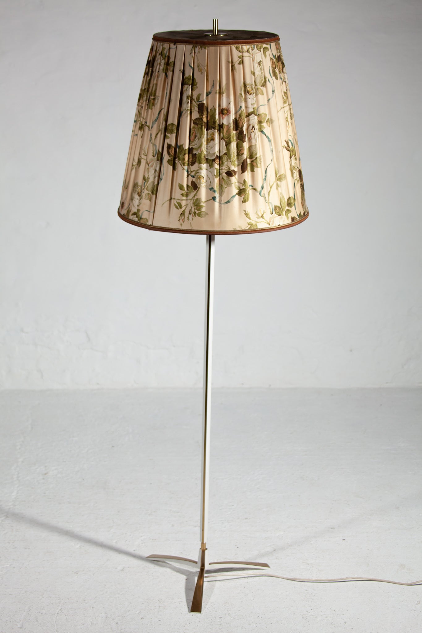 A large brass with accents of white lacquered tripod floor lamp from the fifties with an original print of a floral shade in fabric designed by the Kalmar manufacturer in Austria. The lamp is in excellent condition with nice patina on the brass.