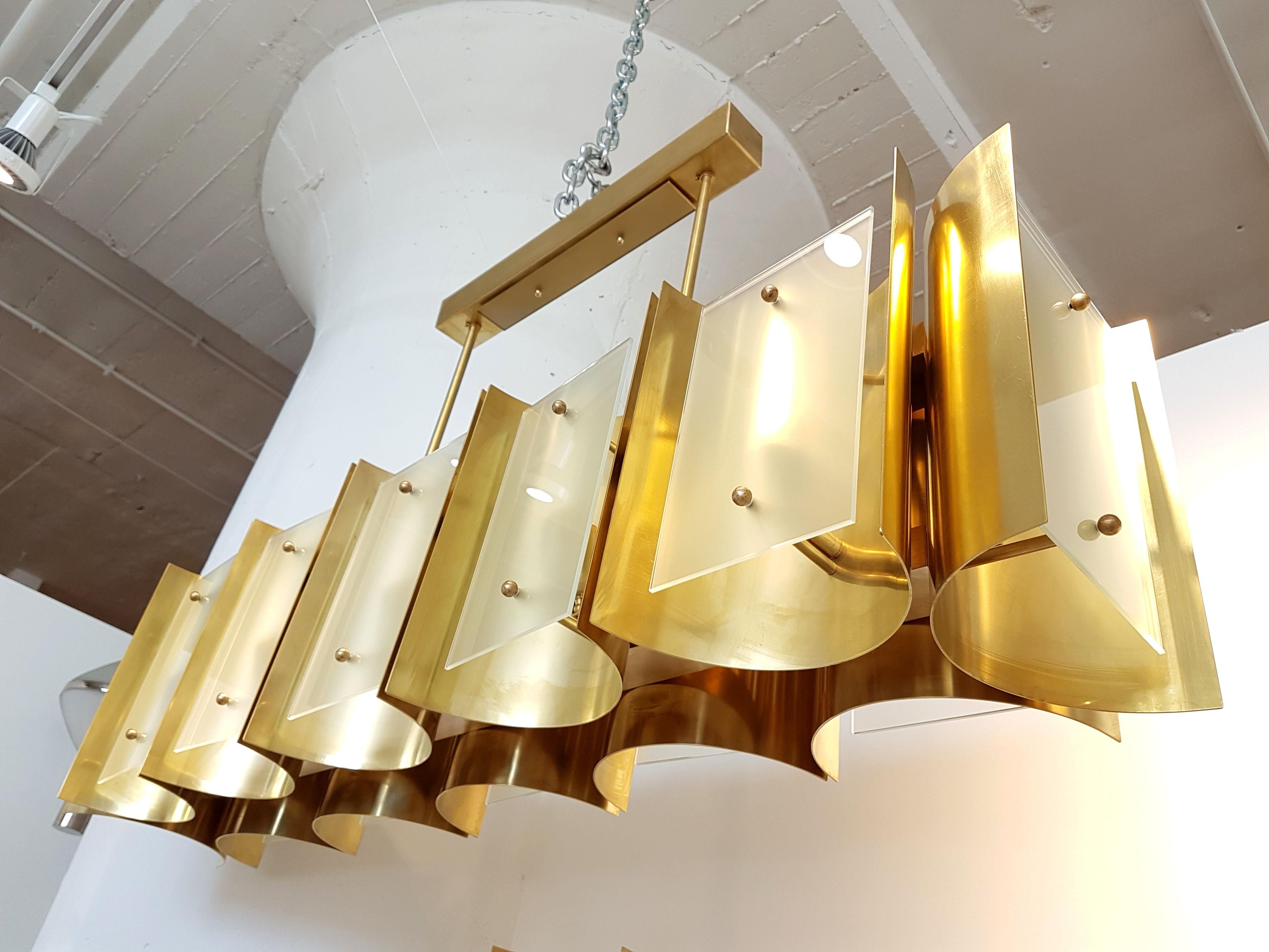 Chandelier or flush mount light, made of 12 polished brass sheets, curved, nesting the light and covered up by a frosted glass. 
Rectangular shape, with 12 candelabra base lights,
1 chandelier available.
Perfect over a table/kitchen