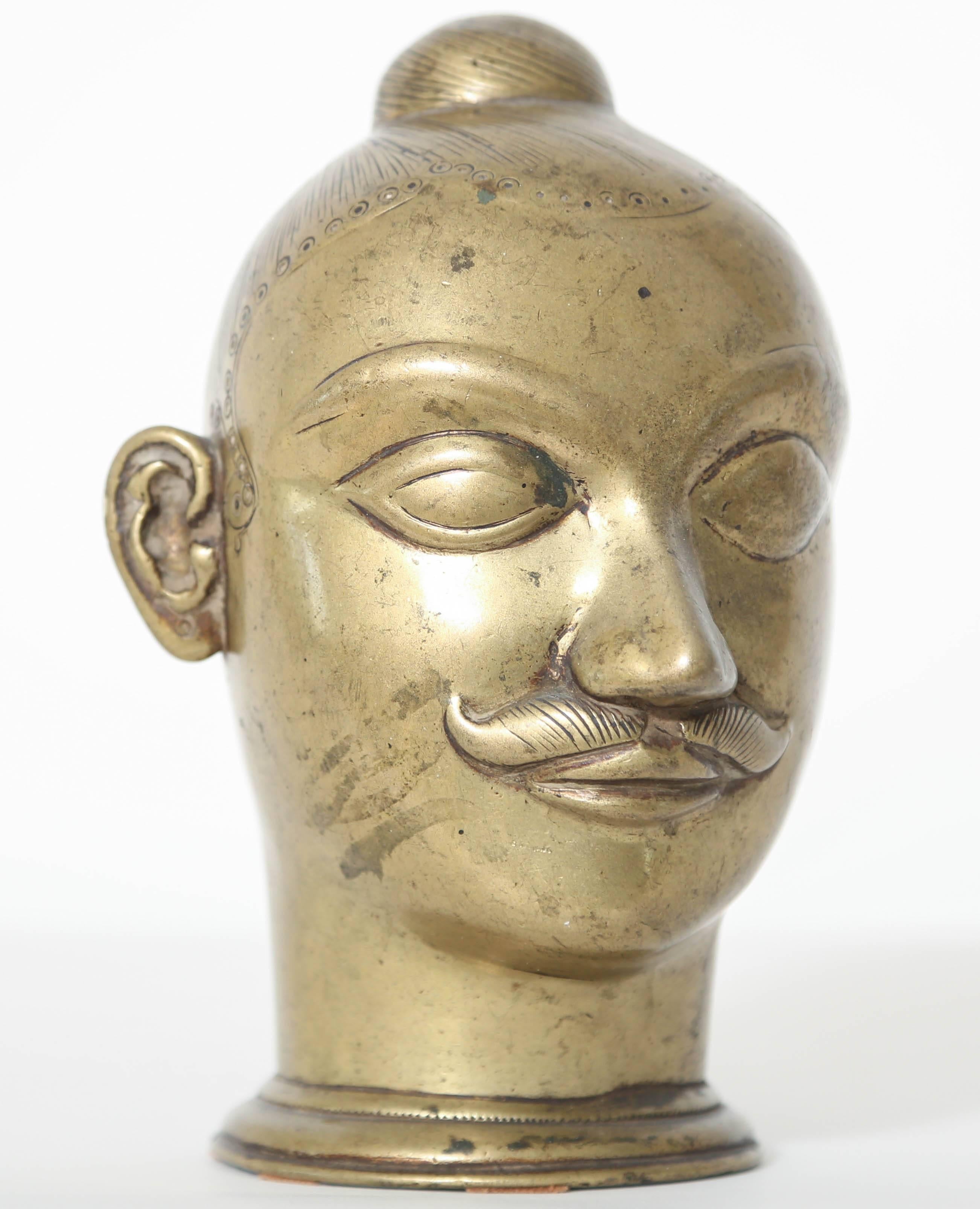 This brass mustachioed head with incised hair in a tight bun was intended to cover a sacred lingam, a symbol of the energy of God, worshipped throughout India. This fine example is from Western India, probably Maharashtra, 18th-19th century.