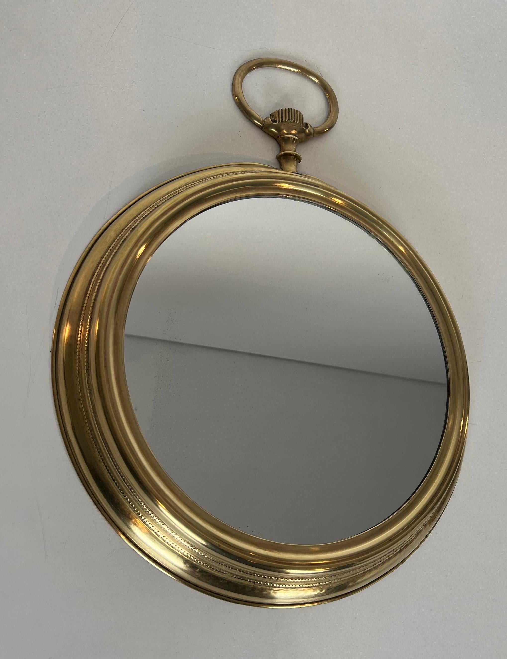 Questo grande specchio che mostra un orologio da tasca è realizzato in ottone con uno specchio rotondo al centro. Questa è un'opera francese. Circa 1970