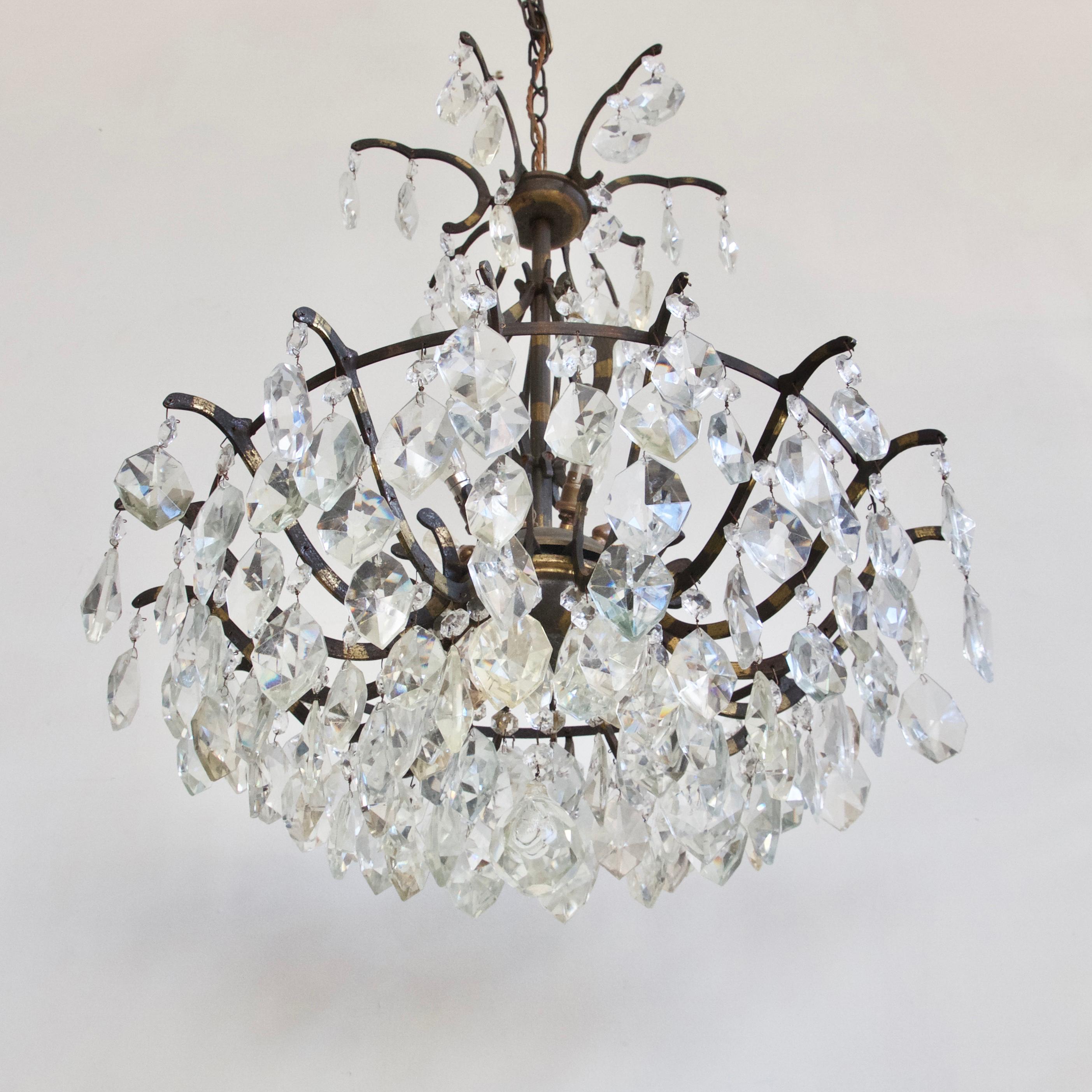 A large brass multi-arm chandelier with a simple brass frame and hand-cut crystal drops. A French 1920s chandelier with inner hidden lamps. The chandelier is a basket shape with a central stem and upper scallops holding more crystal drops. The