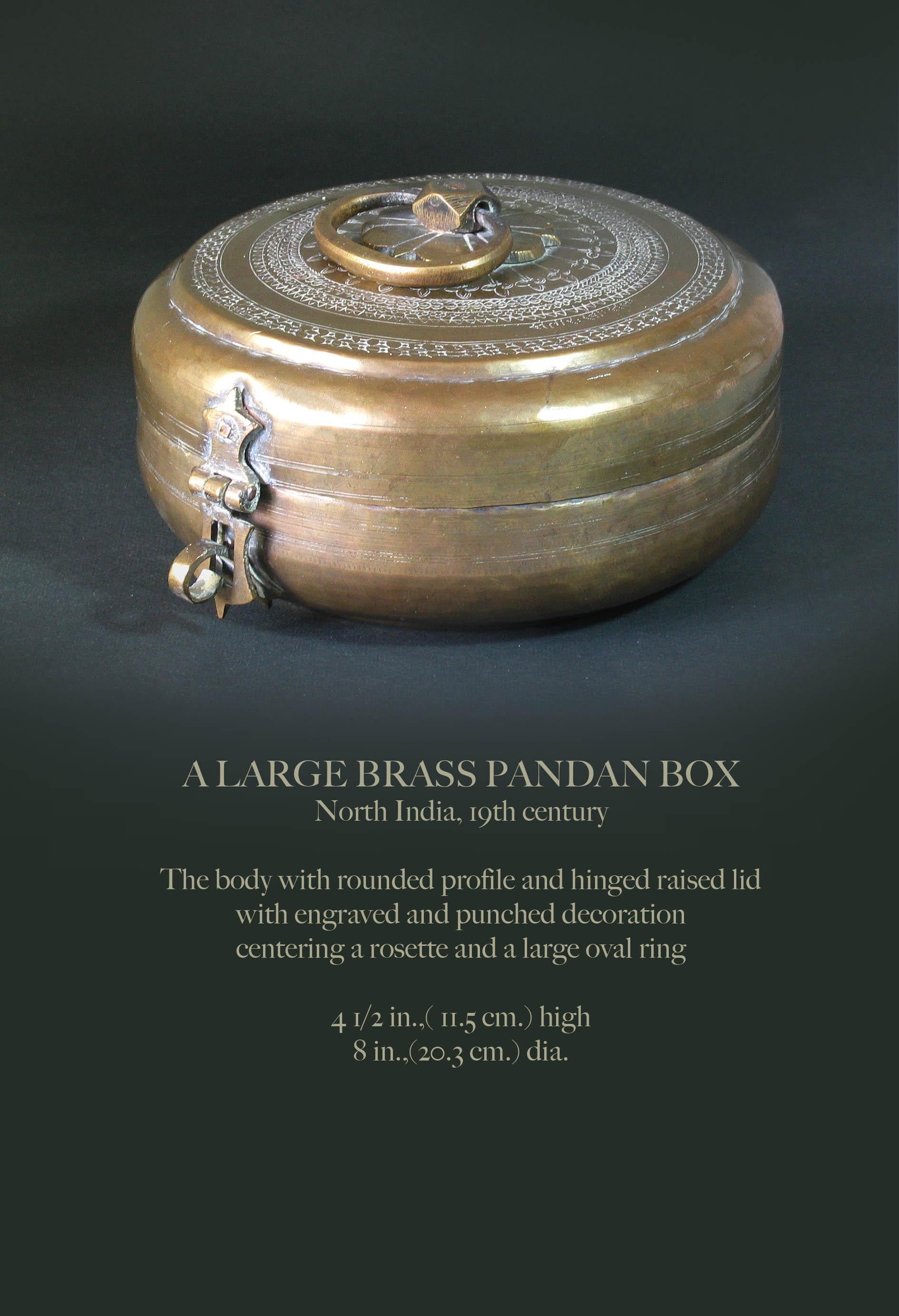 A large brass pandan box
North India, 19th century

The body with rounded profile and hinged raised lid
with engraved and punched decoration
centering a rosette and a large oval ring.

Measures: 4 1/2 in.,( 11.5 cm.) high.
8 in.,(20.3 cm.)