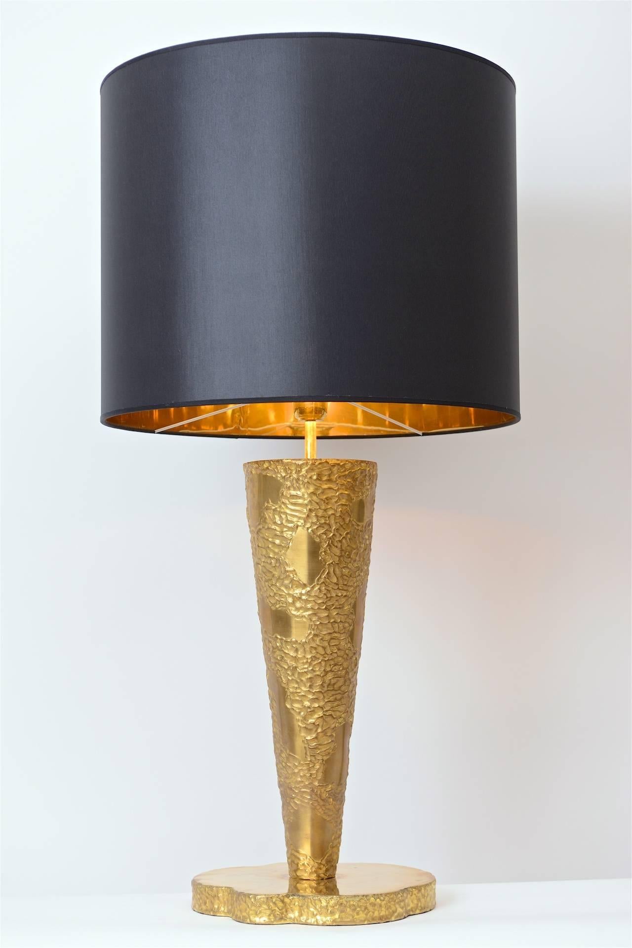 A wonderfully impressive sculptural brass table lamp in the manner of Angelo Brotto, Italy, circa 1970. Its large tapered stem sits on a thick freeform base and is complemented by a beautiful cotton shade with gold coloured inner lining. Completely