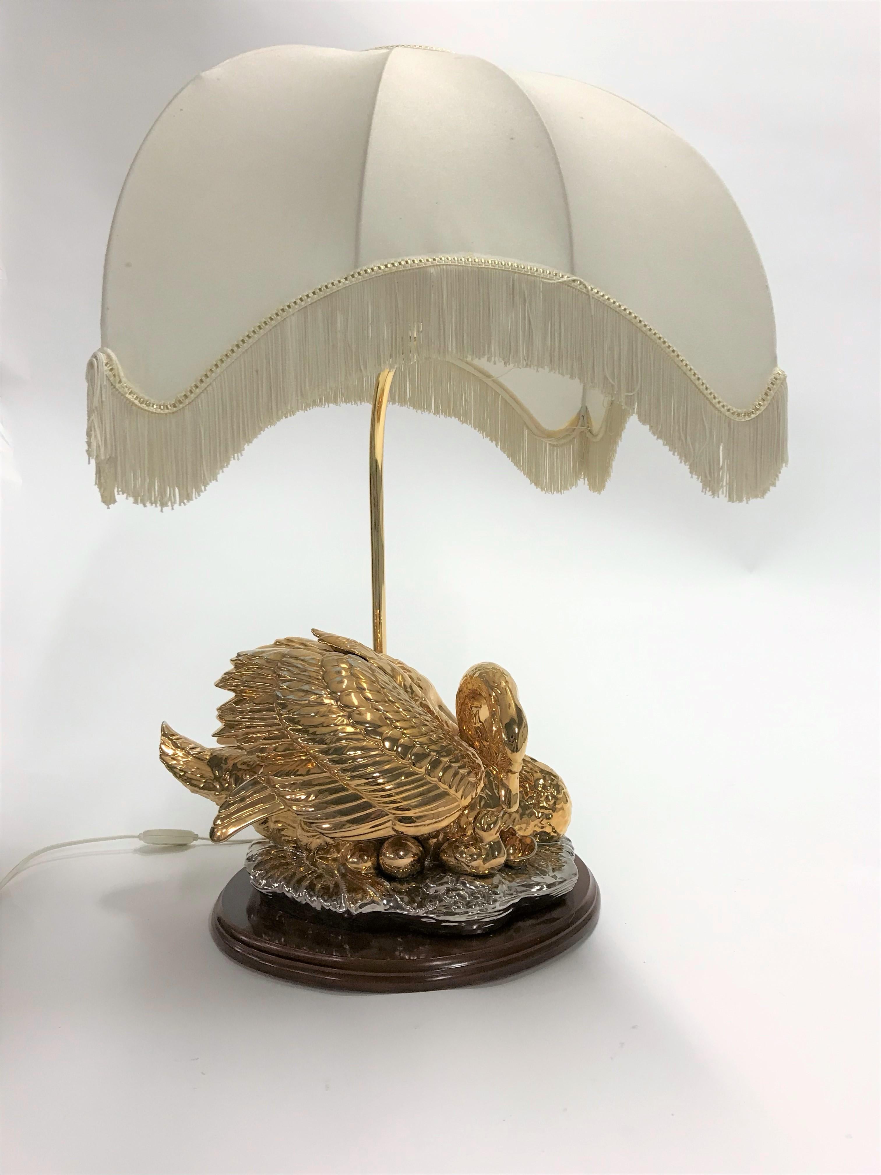 Vintage oversized brass table lamp depicting a sitting swan with a baby swan and eggs.

The sculpture is made of brass and is mounted on a wooden base.

Comes with a huge fabric shade supported by a brass rod.

1960s, Italy

The lamp works