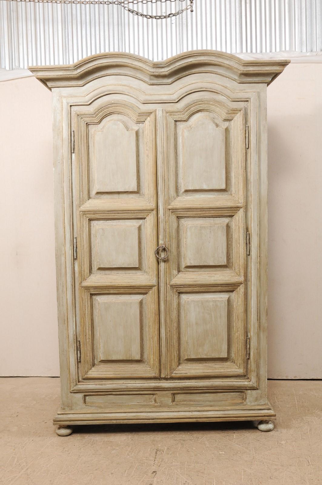 A large sized Brazilian painted wood storage cabinet from the mid-20th century. This vintage cabinet from Brazil features a thickly molded, double hooded pediment, atop two decoratively carved raised panel doors, and is presented upon bun style