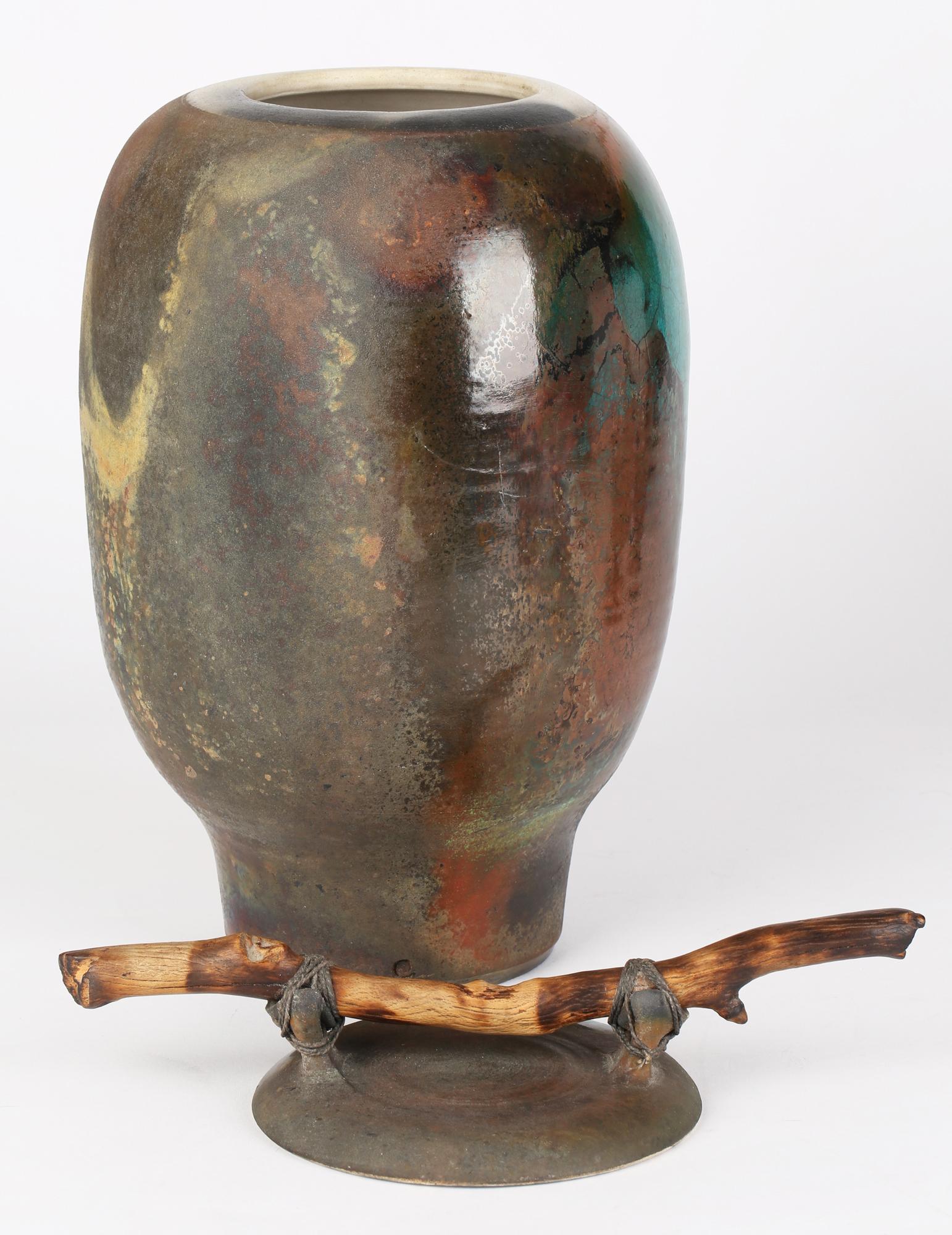 A large and very impressive British attributed studio pottery raku glazed lidded jar with drift wood handle signed CR and dating from the 20th century. The jar hand thrown in white clay stands on a narrow flat round base with a narrow lower section