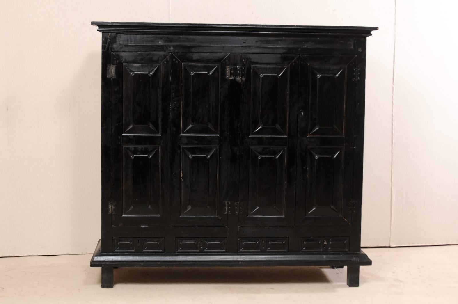 A British Colonial cabinet from the mid-20th century. This vintage storage cabinet from midcentury stands approximately 6.5 ft tall and just over 6 ft wide. It features four carved panel doors, revealing the interior shelving within, over four