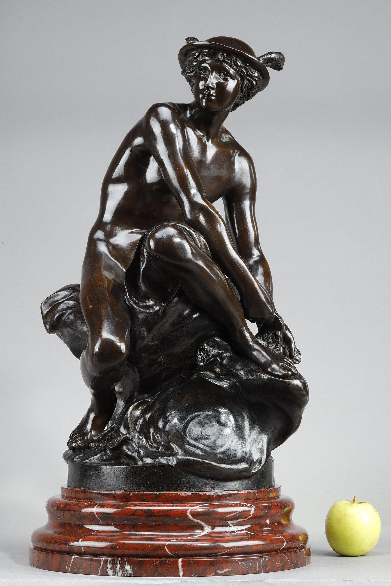 Sculpture en bronze à patine brune représentant Mercure (Hermès), dieu du commerce, des voleurs et messager des dieux, assis sur un rocher en train de nouer sa talonnette ailée. Il porte un pétase, un chapeau ailé, et son caducée repose sur le sol.