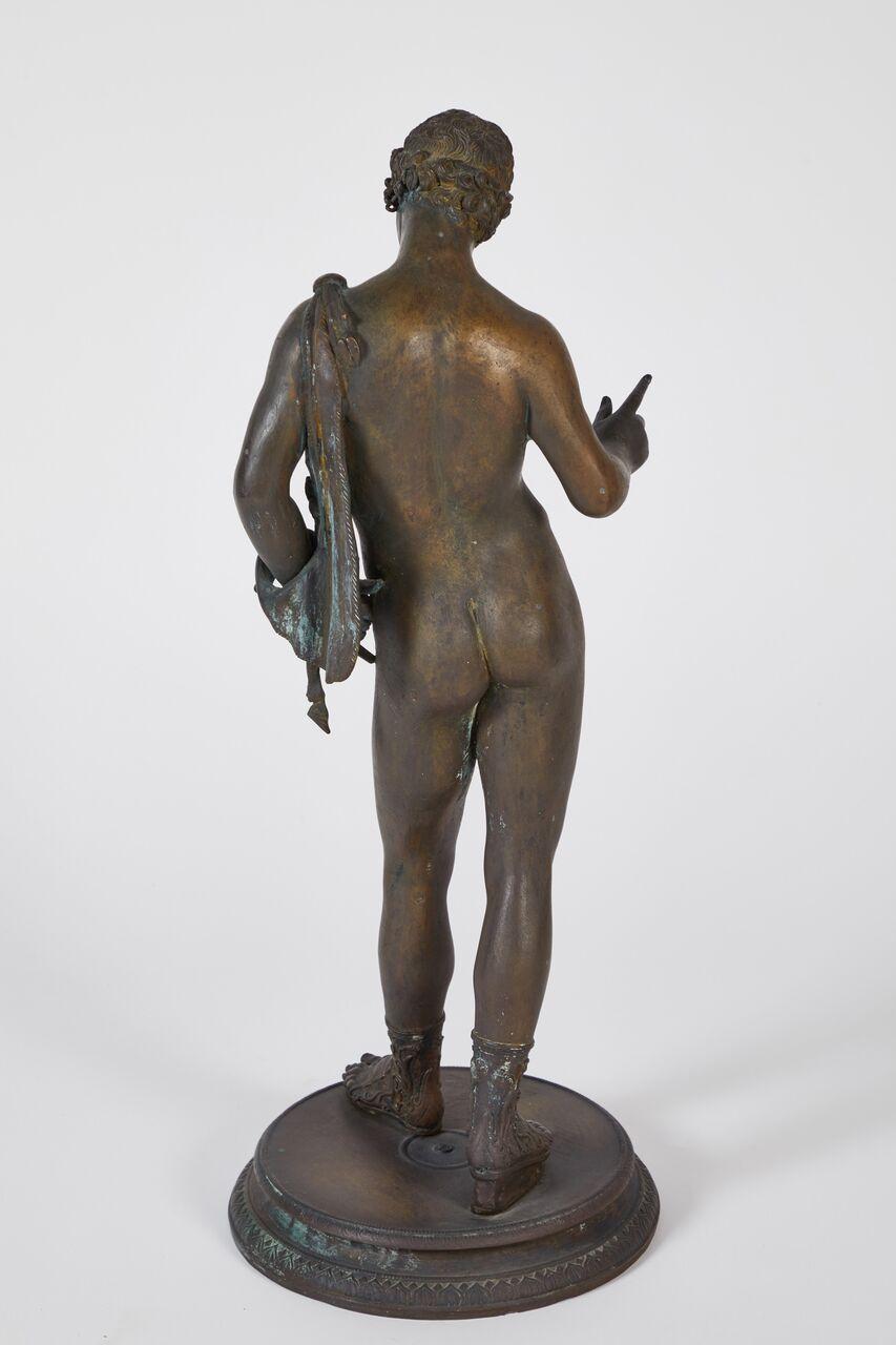 Classical bronze sculpture of Narcissus. The bronze is shown nude except for a pair of sandals, standing on a circular plinth with his head bowed and an arm extended, an animal skin draped over one shoulder.
Modeled after the original Narcissus