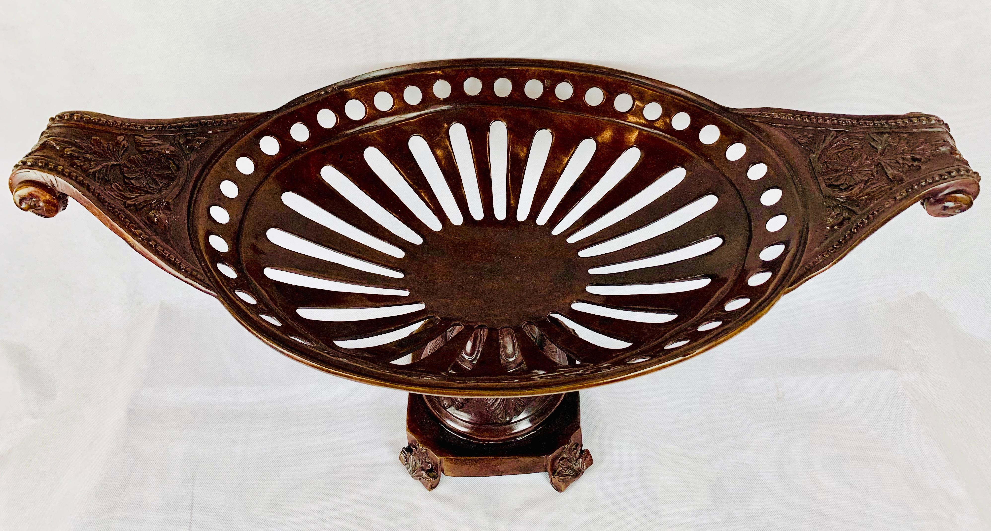 Large bronze footed basket. The oval basket is pierced with a symmetrical pattern. The scrolled handles are deeply engraved with flowers and acanthus leaves bordered with a bead pattern. The round stem or neck covered with more acanthus leaves rests