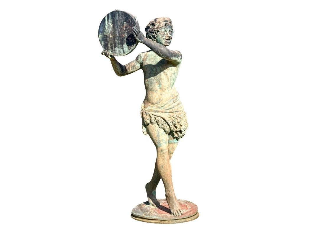 Un'imponente statua da giardino in bronzo di grandi dimensioni che raffigura un giovane classico che indossa una fascia di vello intorno ai fianchi, in posa che cammina su una base circolare con un tamburello sollevato in alto. Il bronzo è montato