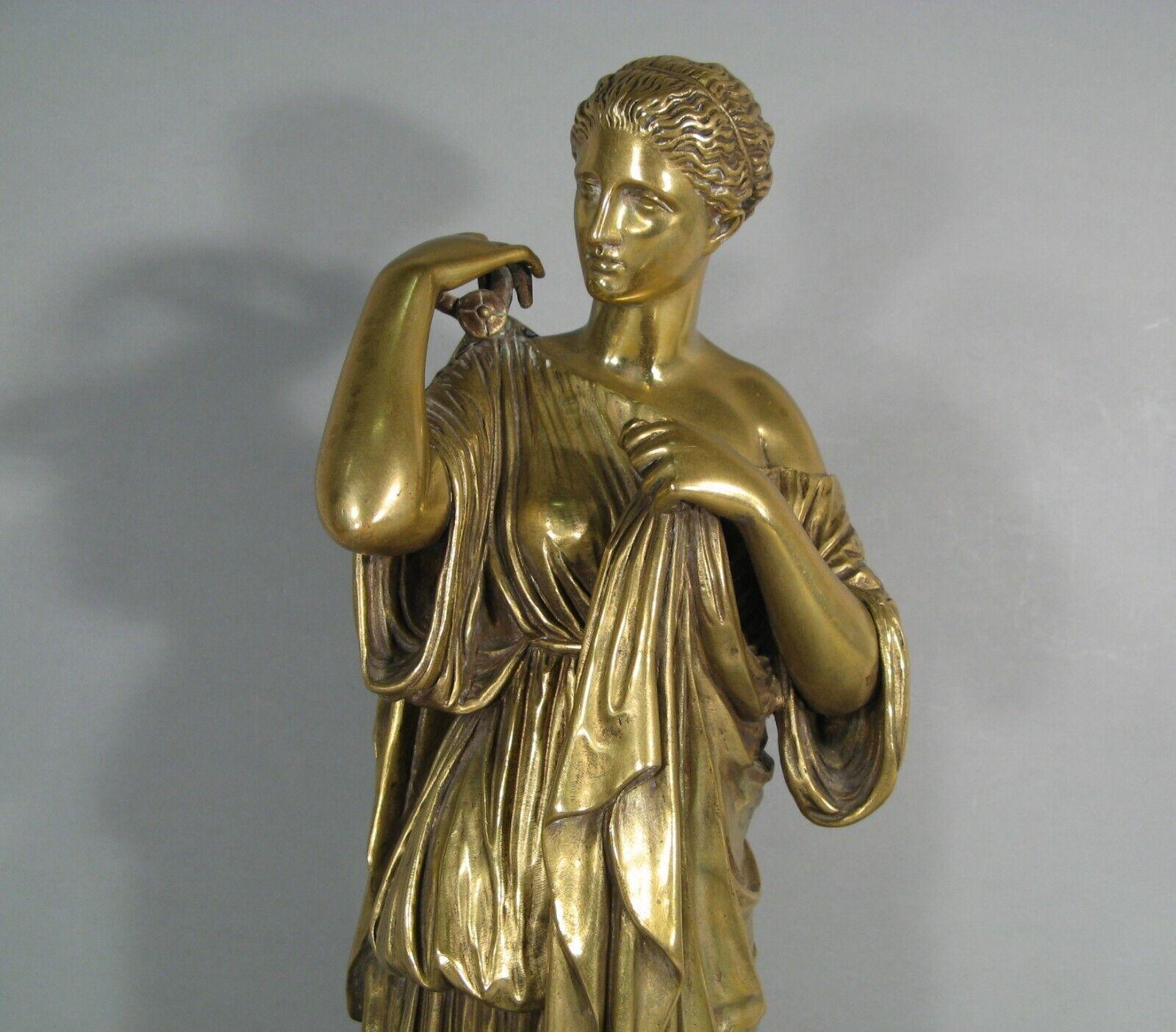 Esta gran escultura de bronce representa a Artemisa, la diosa griega de la caza, en el acto de abrocharse el manto. La pieza es una reproducción finamente elaborada de la estatua clásica conocida como Diana de Gabies, atribuida al antiguo escultor