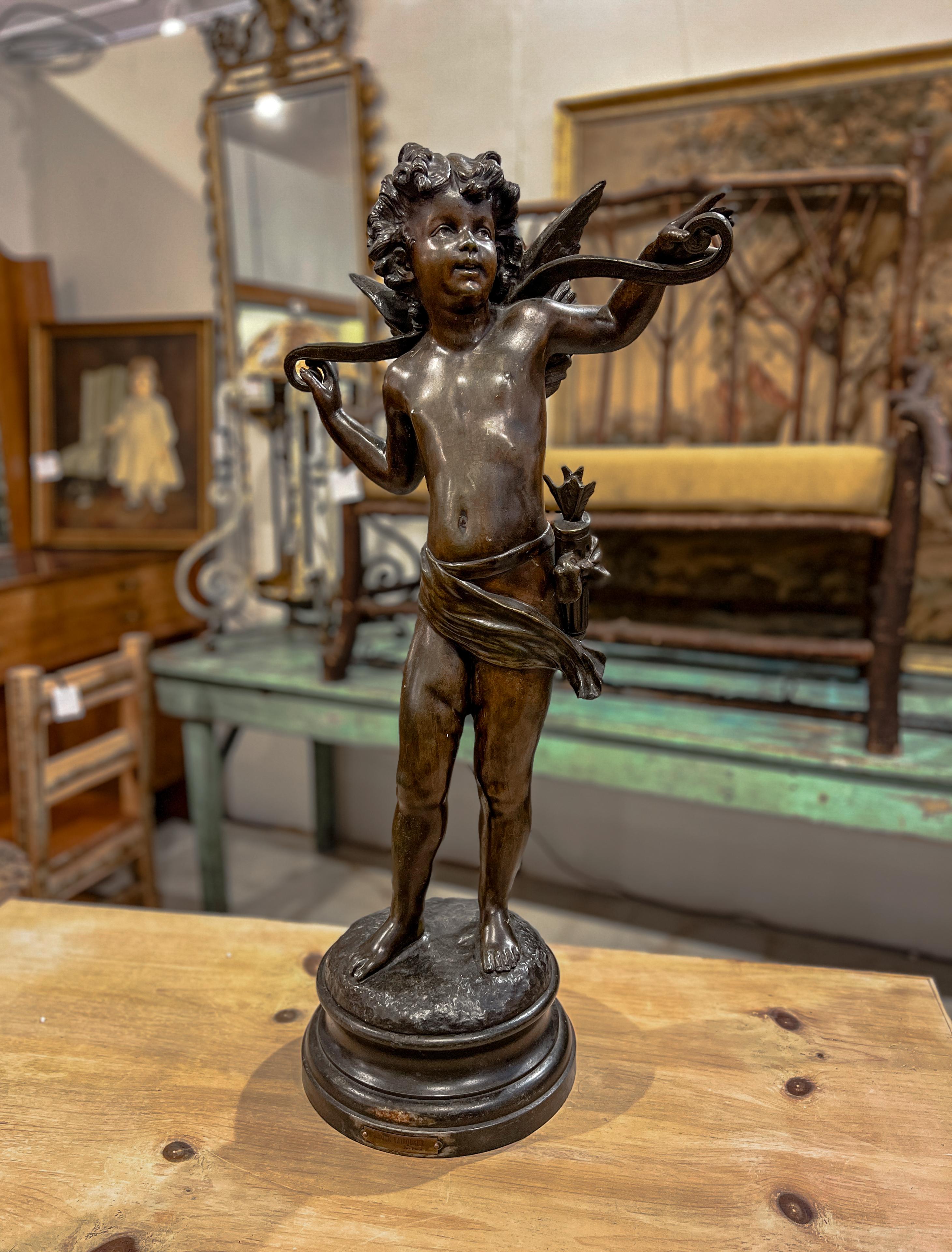 Large bronze-color statue of Cupid. The plaque on the base says 