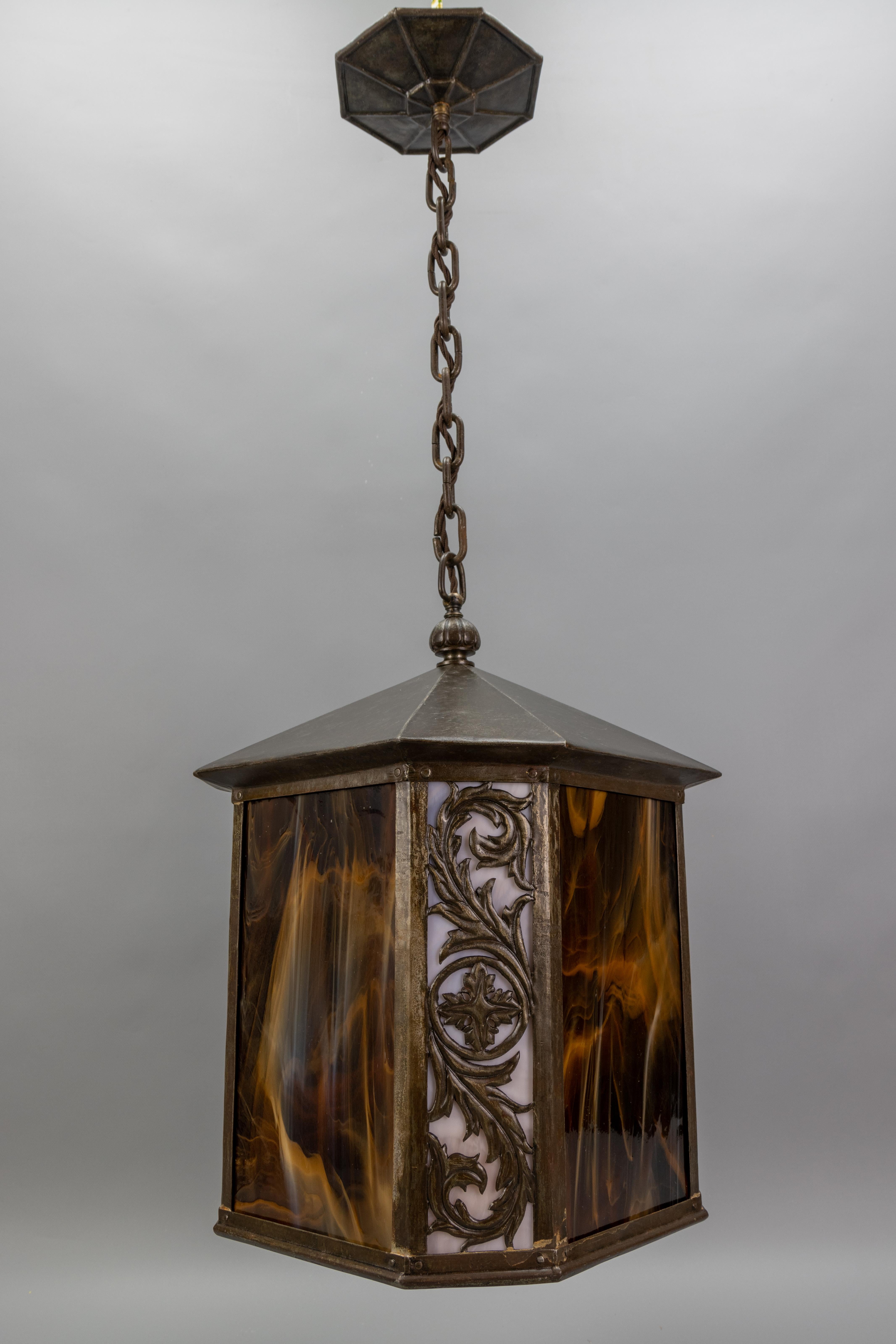 Cette impressionnante lanterne de couloir de grande taille, fabriquée en France dans les années 1920, à l'époque des Arts and Crafts, présente un design rare composé de verre Tiffany marron et beige combiné à du métal. 
La lanterne présente un cadre