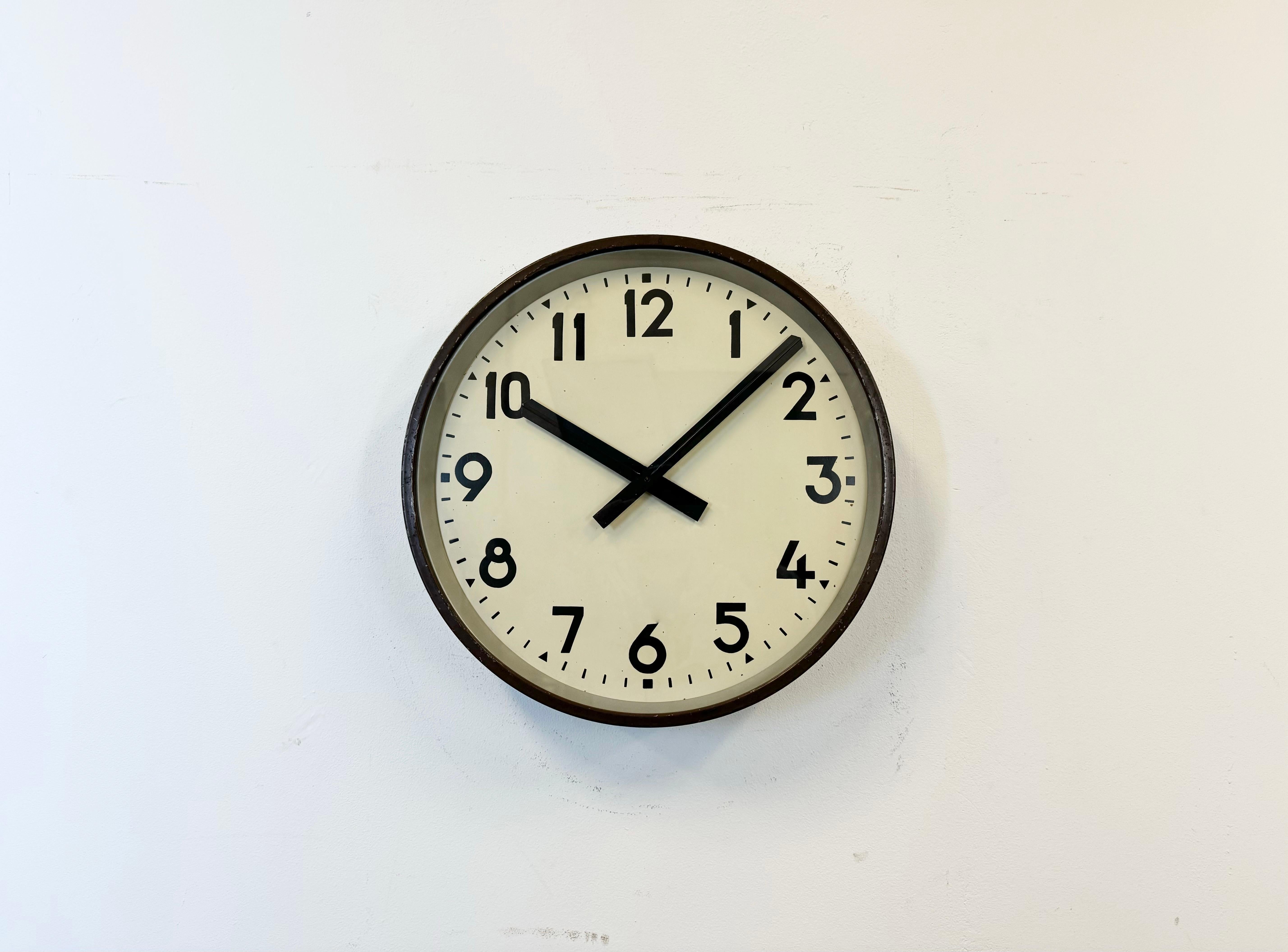 This factory wall clock was produced in former Czechoslovakia during the 1950s. It features a brown metal frame, iron dial, aluminum hands and clear glass cover. Former electrical slave clock has been converted into a battery-powered clockwork and
