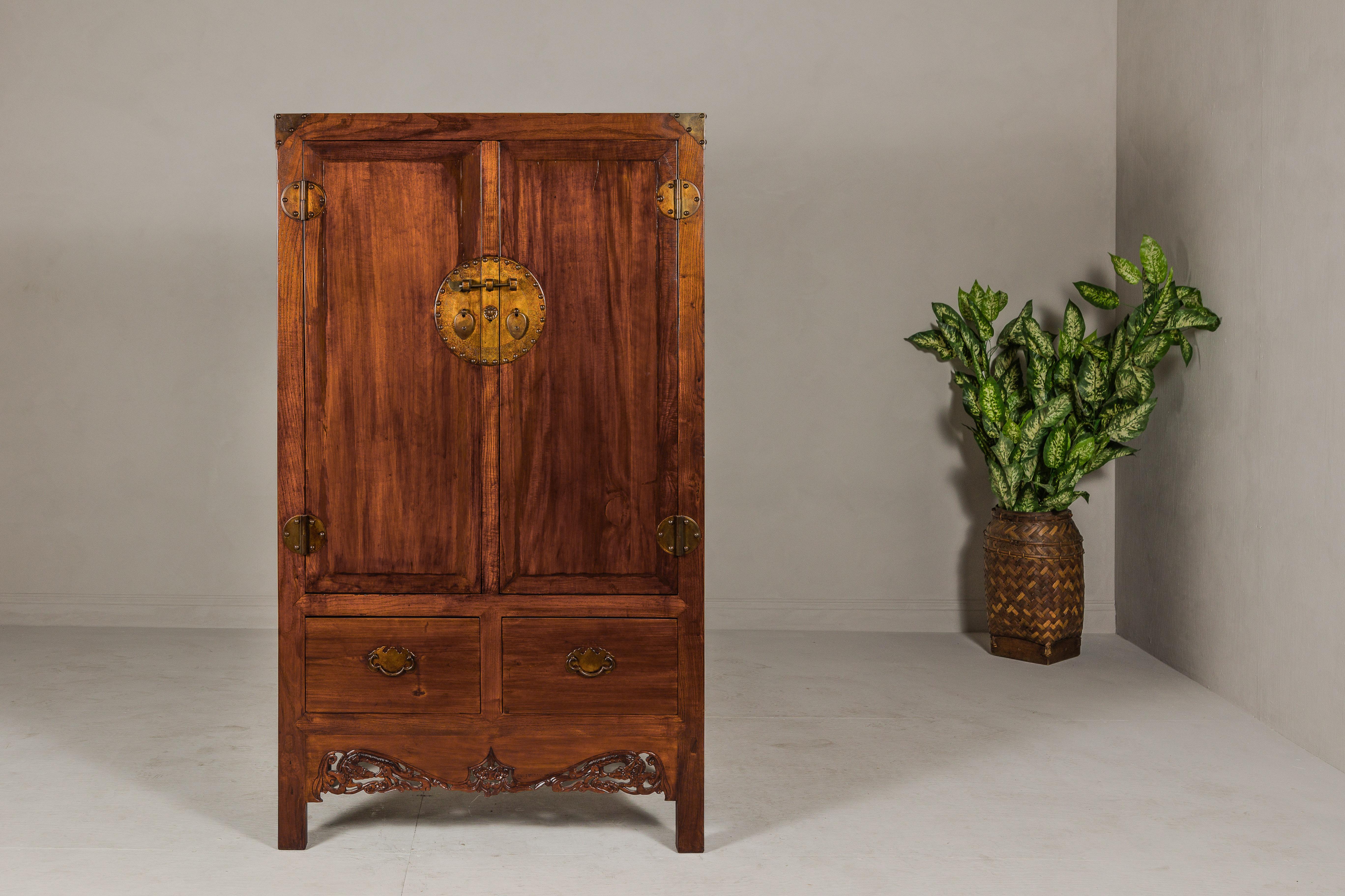 A Chinese Qing Dynasty period large elwood cabinet from the 19th century with brown lacquer, carved fretwork skirt, round medallion hardware, two exterior drawers, interior shelves with hidden drawers. This Chinese Qing Dynasty period large elwood