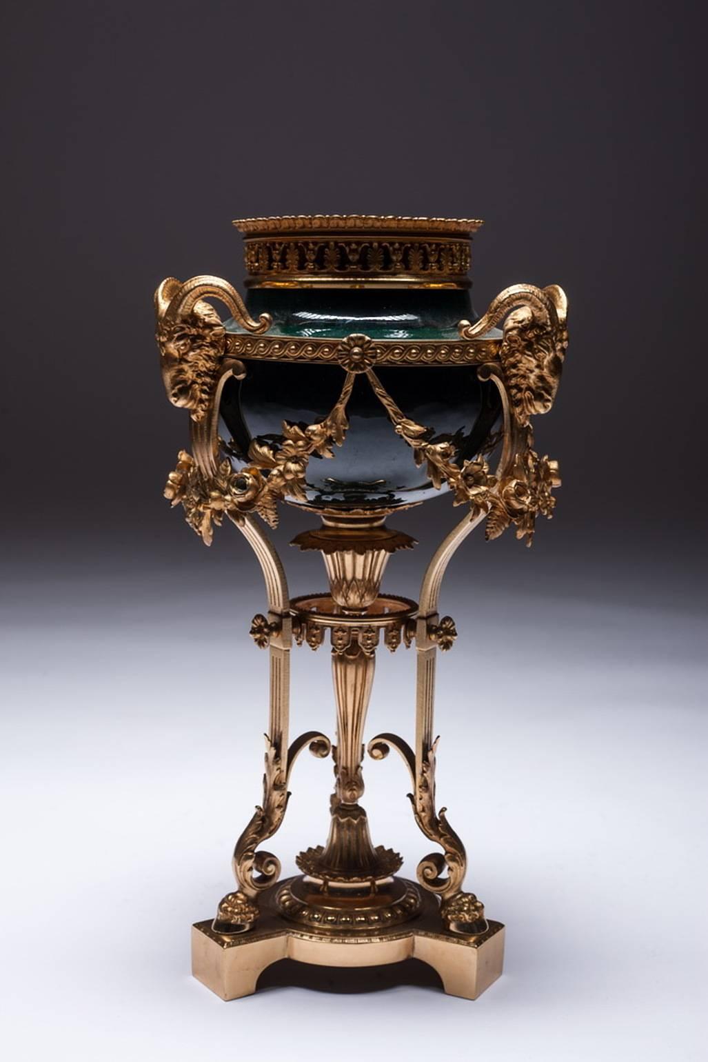 Large Brûle perfume bronze, gilded. Three-sided grooved base. Of them ascending three relief struts with trestles, above naturalistic ram's head. Porcelain half-spherical corpus, centered on struts, with wide, open-worked rim. Slightly domed lid