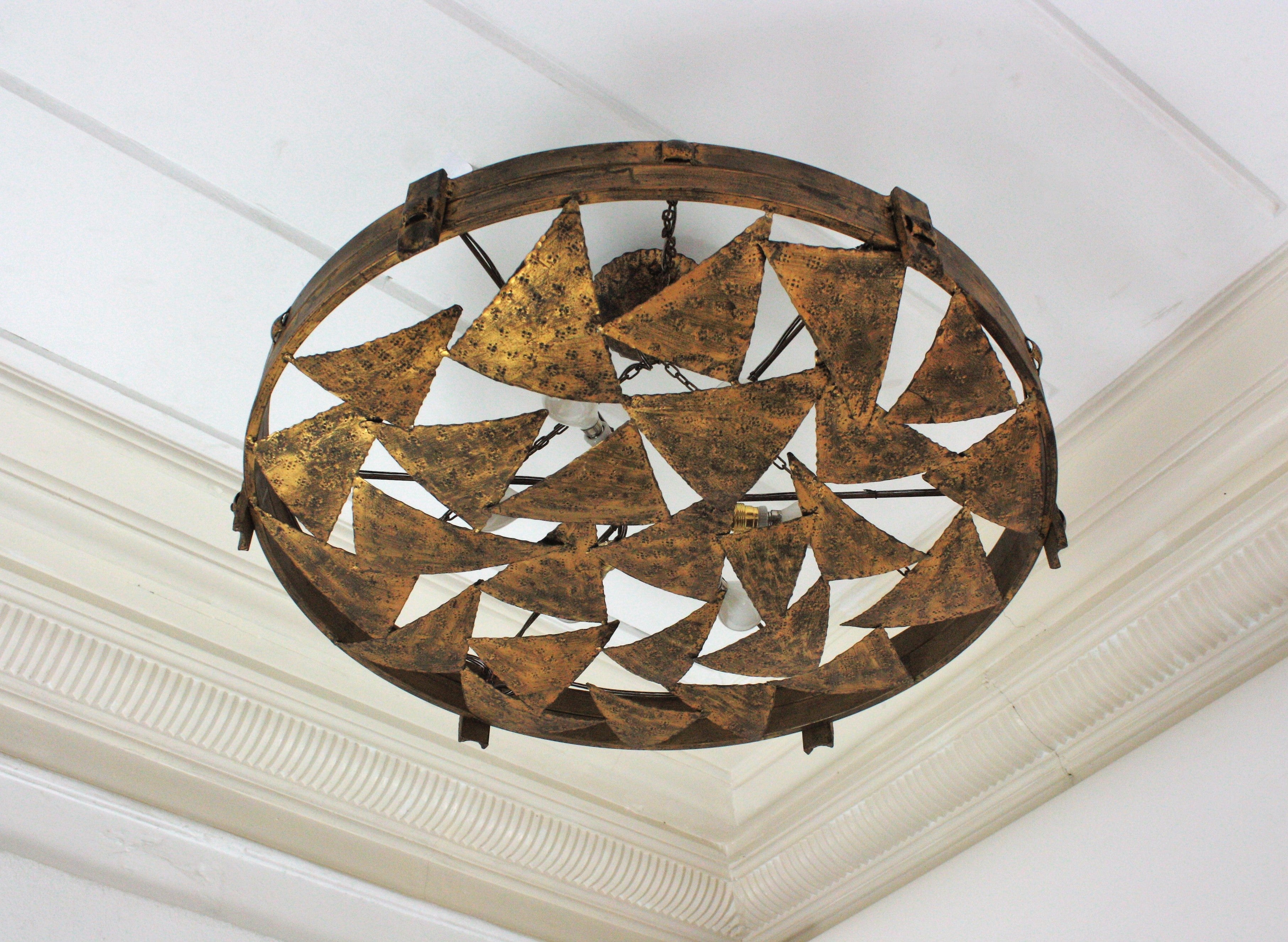 One of a kind Spanish Round Wrought Flush Mount Light Fixture in Gilt Iron. Spain, 1950s.
This monumental ceiling flush mount is entirely made in hand-forged iron and finished in gold leaf gilding.
It features a composition of triangle pieces in