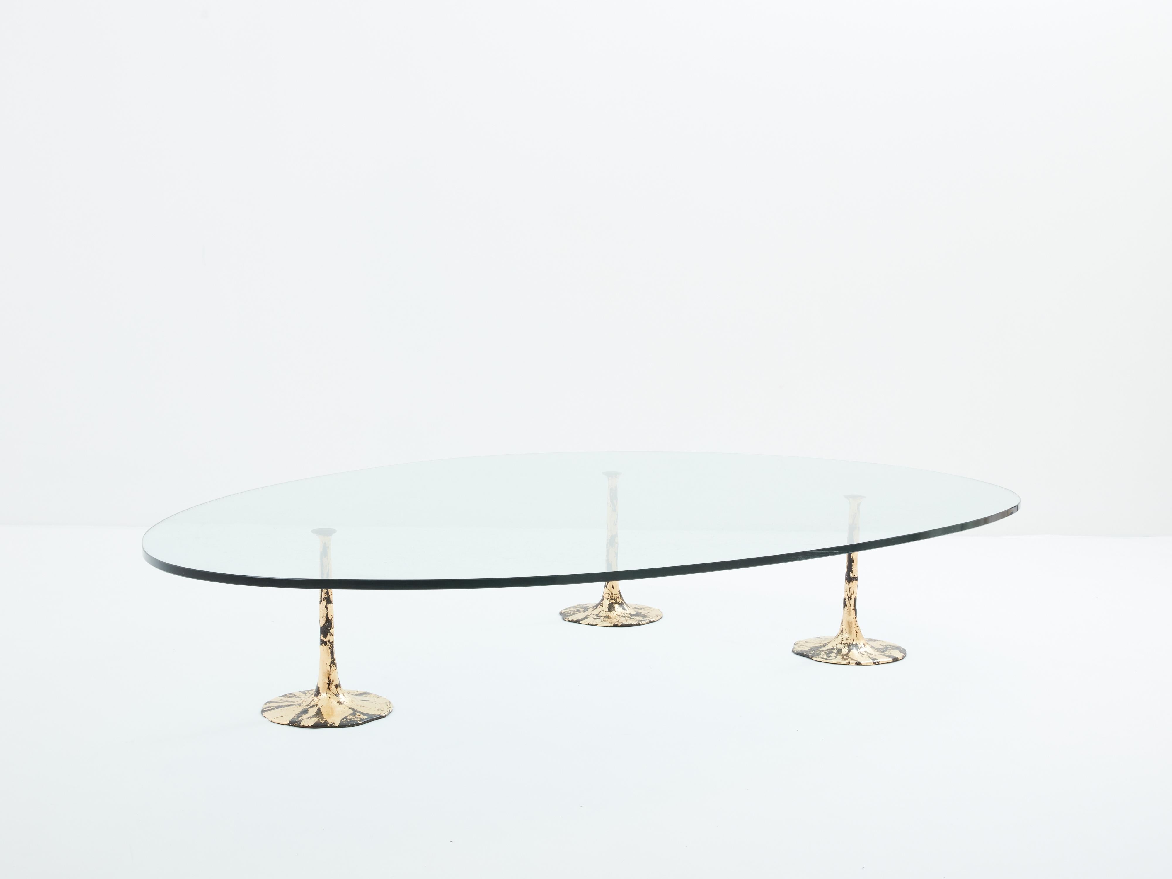 Rare et unique table basse conçue par un designer anonyme français dans les années 1970. Les trois pieds brutalistes réglables sont réalisés en fer forgé patiné et doré, avec une finition à la feuille d'or, avec un plateau en verre épais transparent