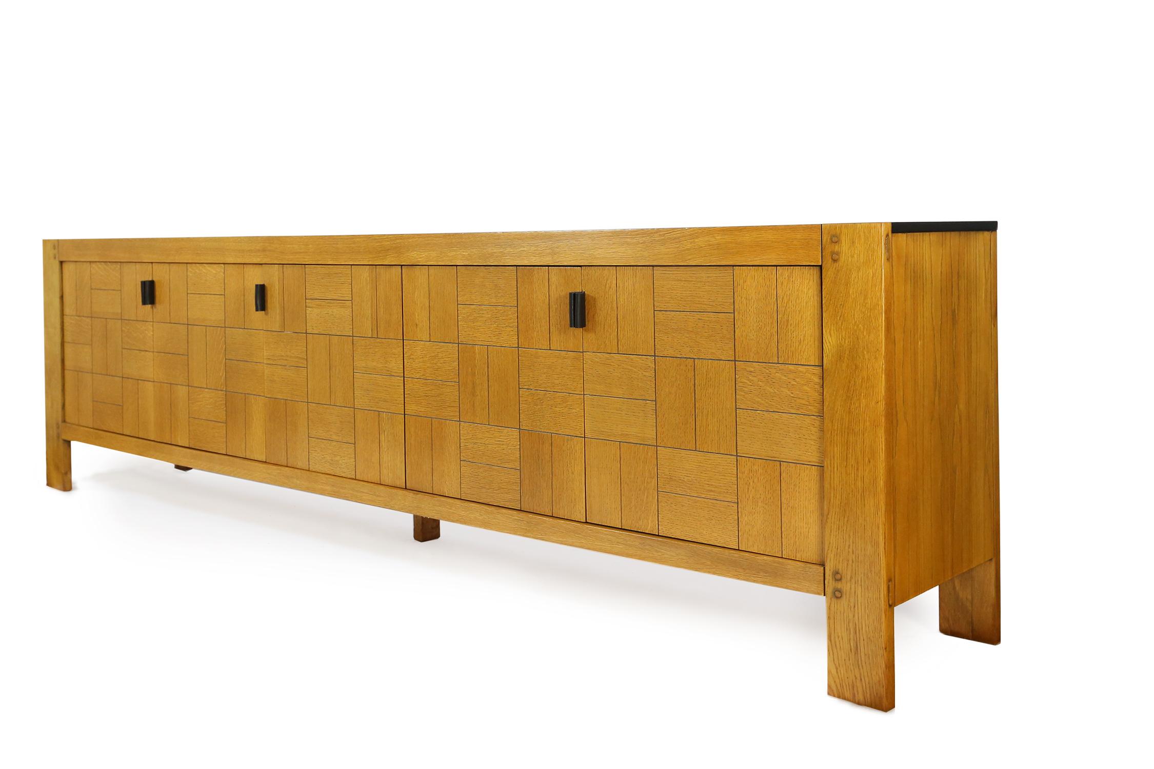 Brutalist sideboard executed in oak. The decorative doors are finished in way that a patchwork is created with a combination of horizontal and vertical inlayed grained oak tiles. The handles are made of black leather and while opening the doors