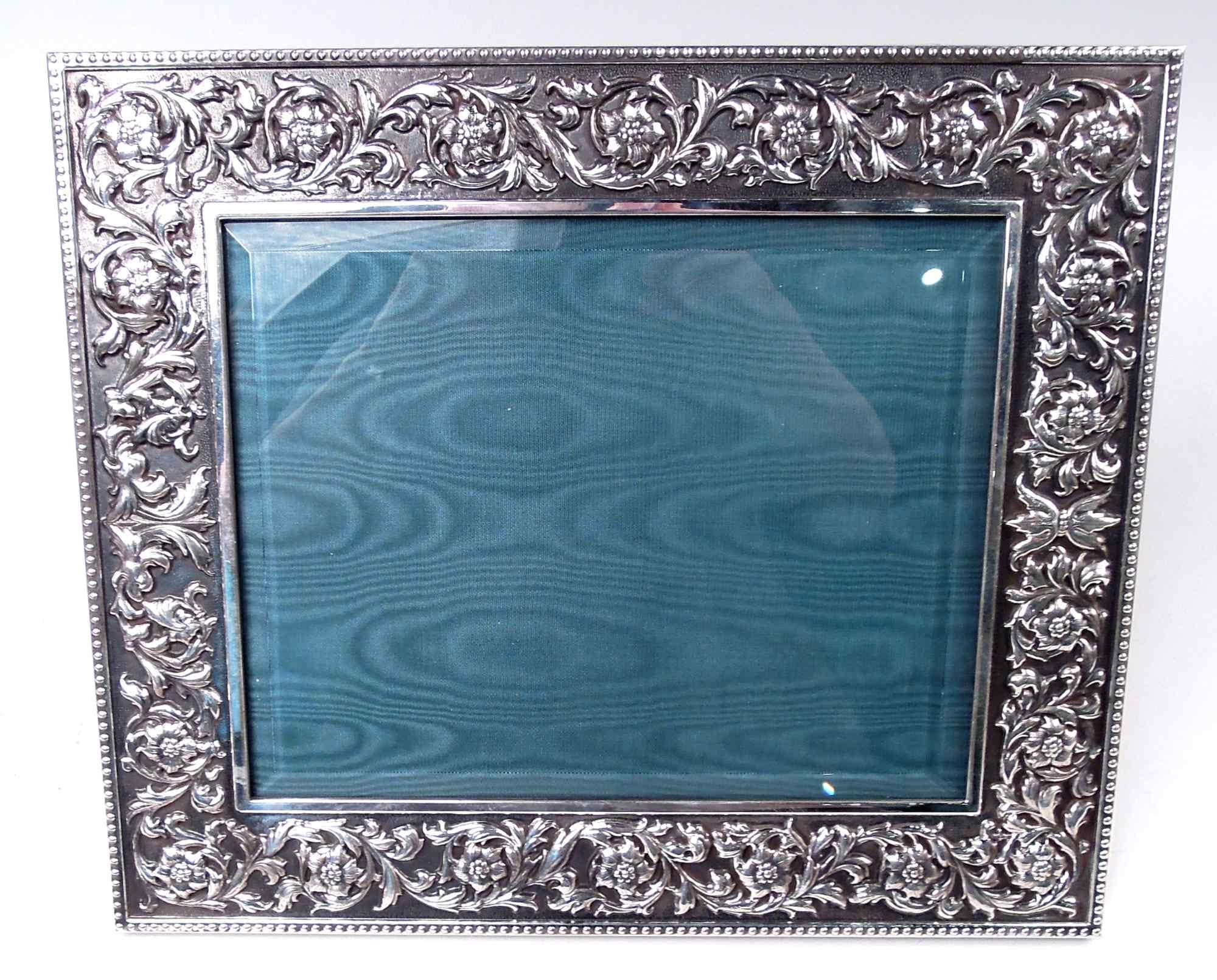Classical sterling silver picture frame. Made by Buccellati in Italy. Rectangular surround. On front, cast rinceaux border on stippled ground; plain flat interior rim and beaded exterior rim. Sides plain. With beveled glass, silk lining, and leather
