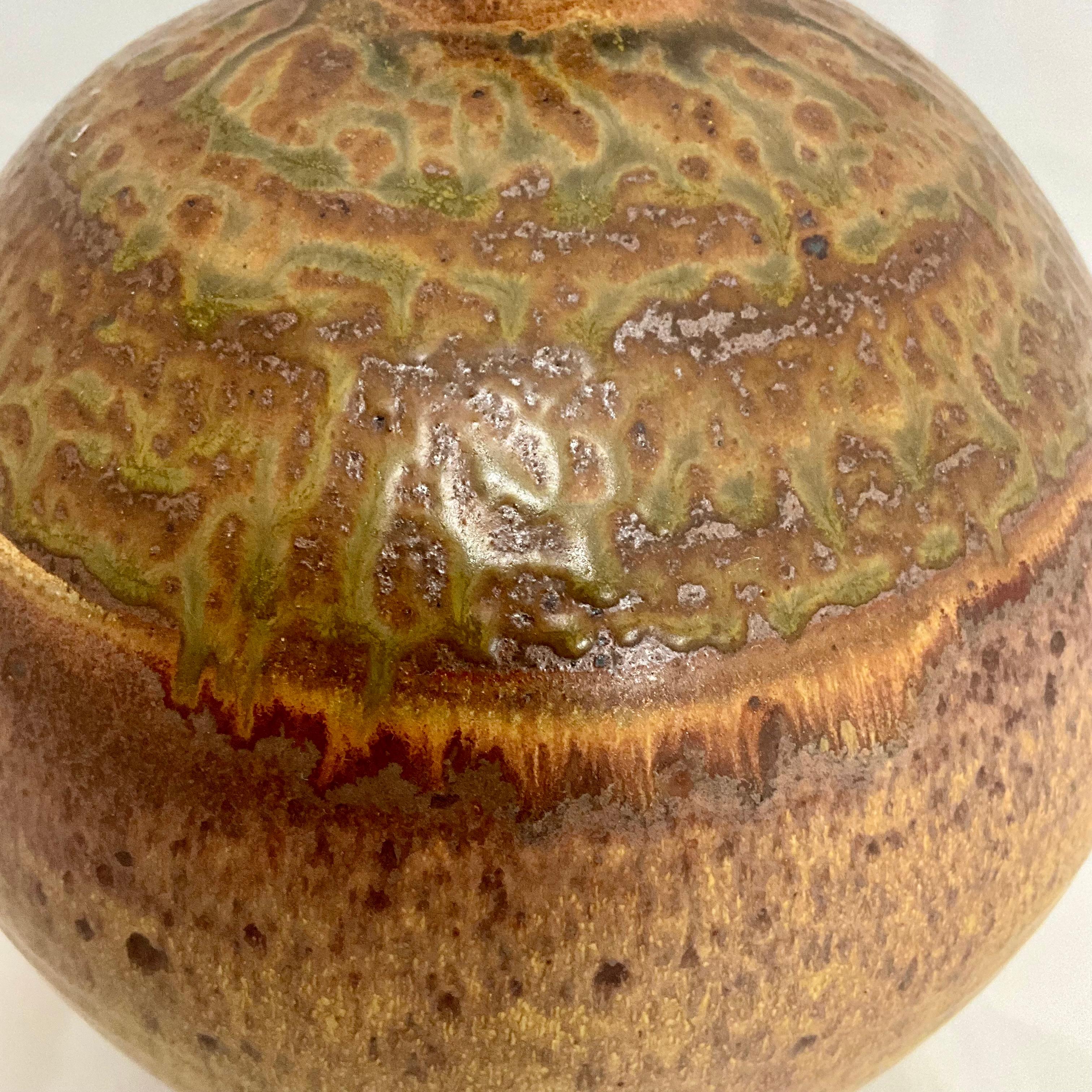 Larger mid century studio pottery vessel hand thrown in hues of mustard, brown and green, the colors darkening as they graduate to the top of the vase. This pieces is signed on the underside with an illegible signature.  No chips or cracks in