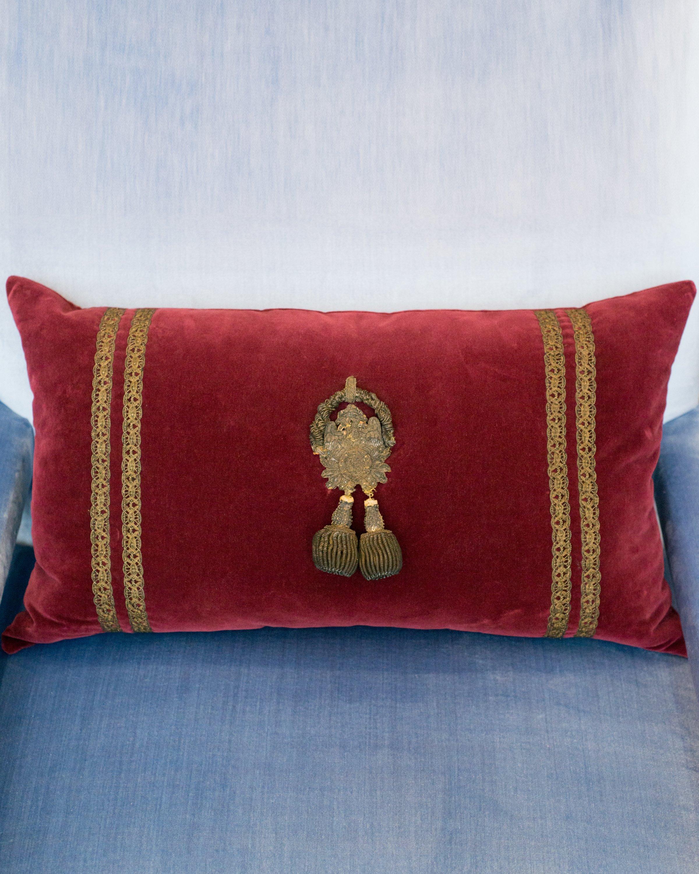 A burgundy velvet ottoman pillow with antique metallic gimp and large metallic beaded tassels.