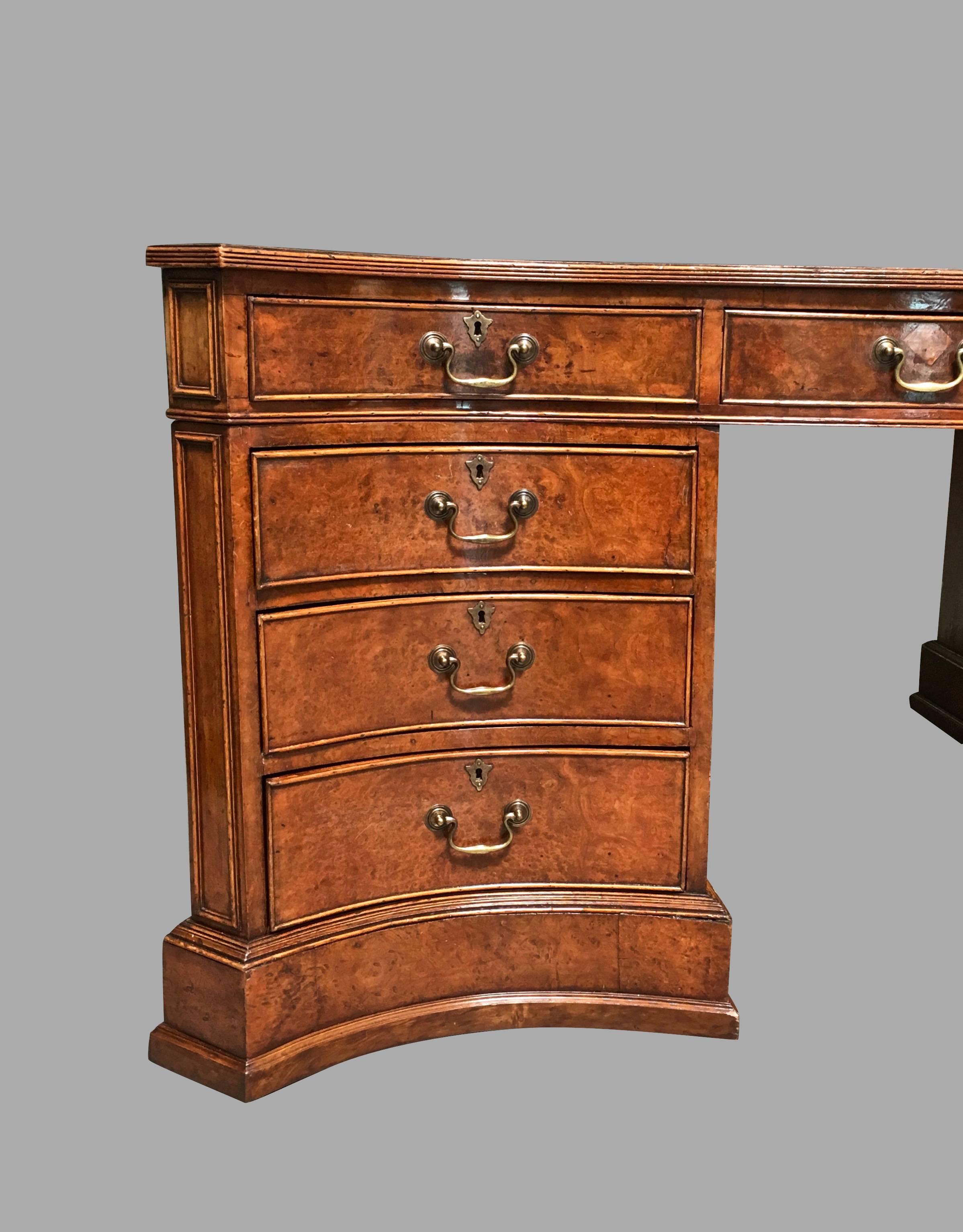 An impressive English Georgian style burl elm serpentine form partners desk of large-scale, the brown gilt-tooled leather top with a molded edge above three frieze drawers, each pedestal with three additional drawers, the reverse with cupboard