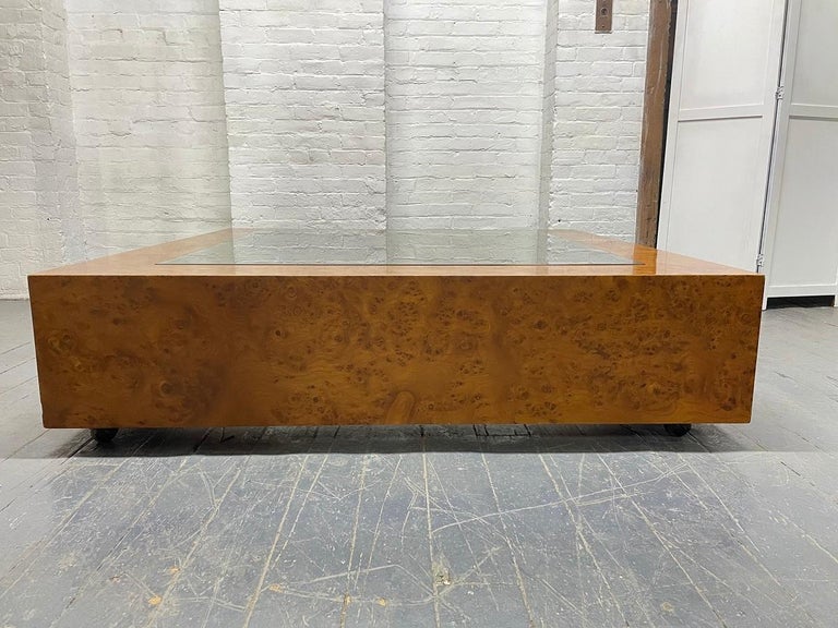 Large burl wood and glass top coffee table. The table has a glass insert, nice burl grain, and the table has casters. Karl Springer style.