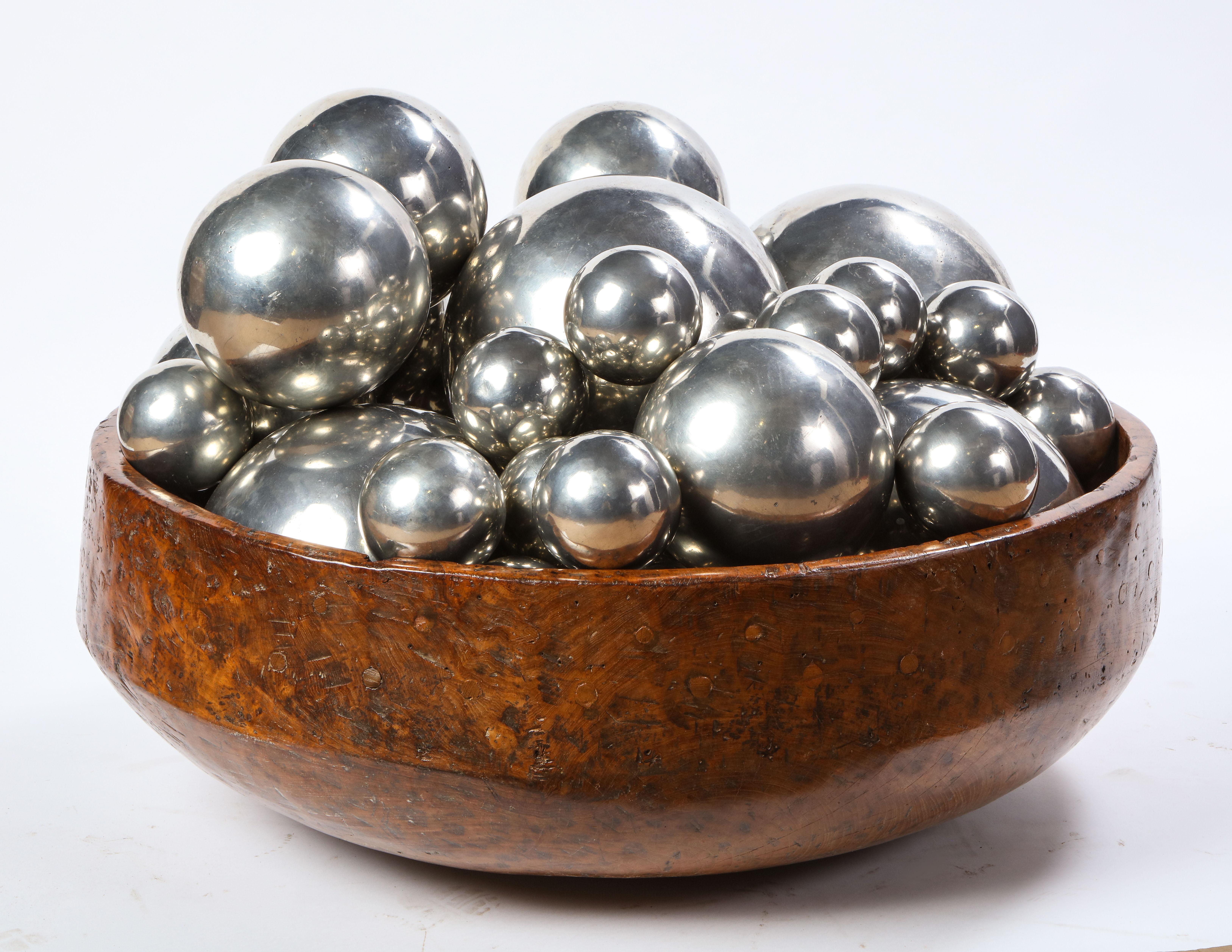 A large carved burl wood bowl from the 20th century. Together with thirty-one large silvered-metal spheres. The rustic-style bowl was carved from a delightfully knotty burl wood specimen and makes a beautiful decorative piece together with the