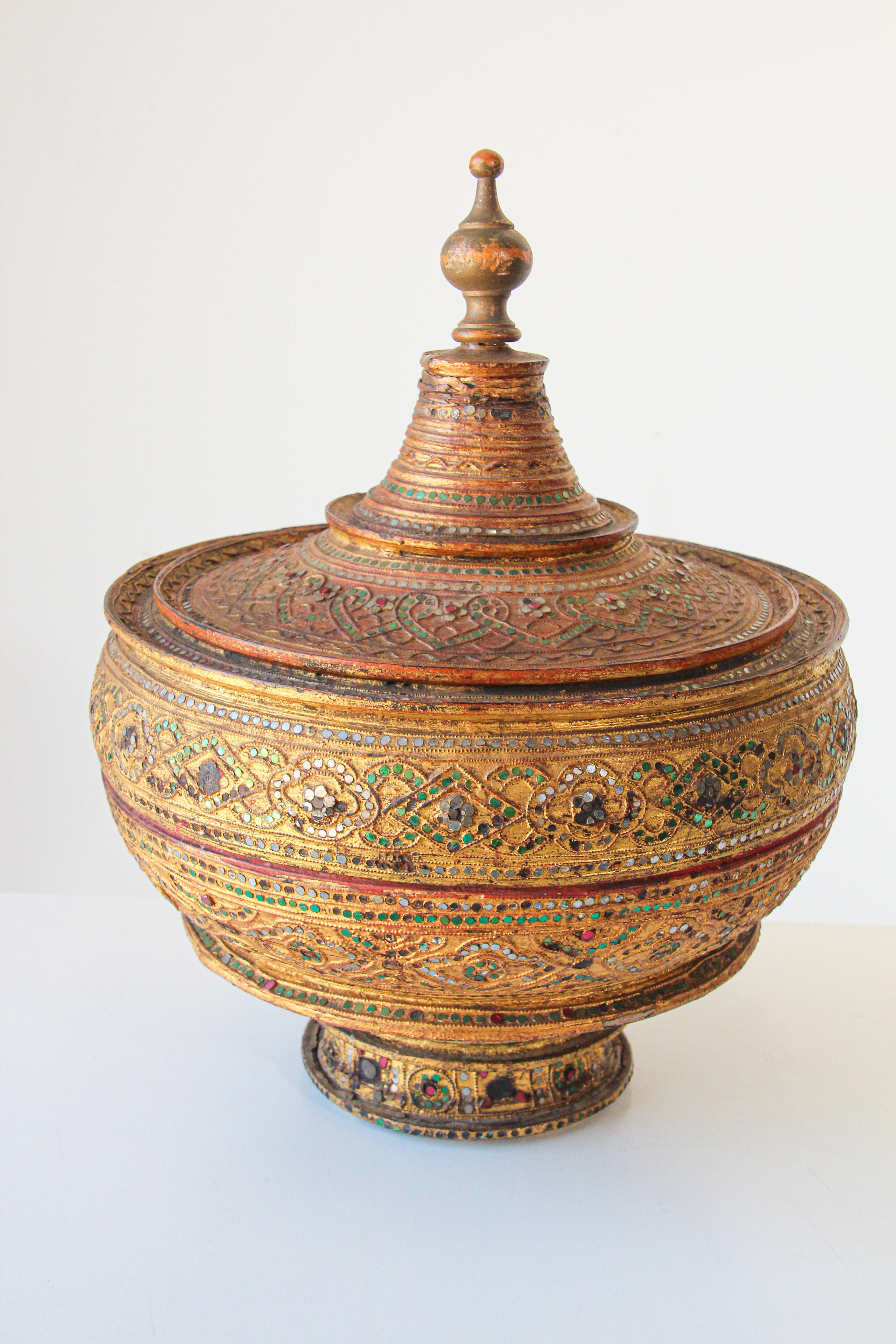 A very large Asian Burmese gilt and lacquered wood bamboo offering vessel, container adorned with mirror and jewels colored gems with a conical removable top.
Burmese temple offering covered box, with a red lacquer interior, richly decorated with