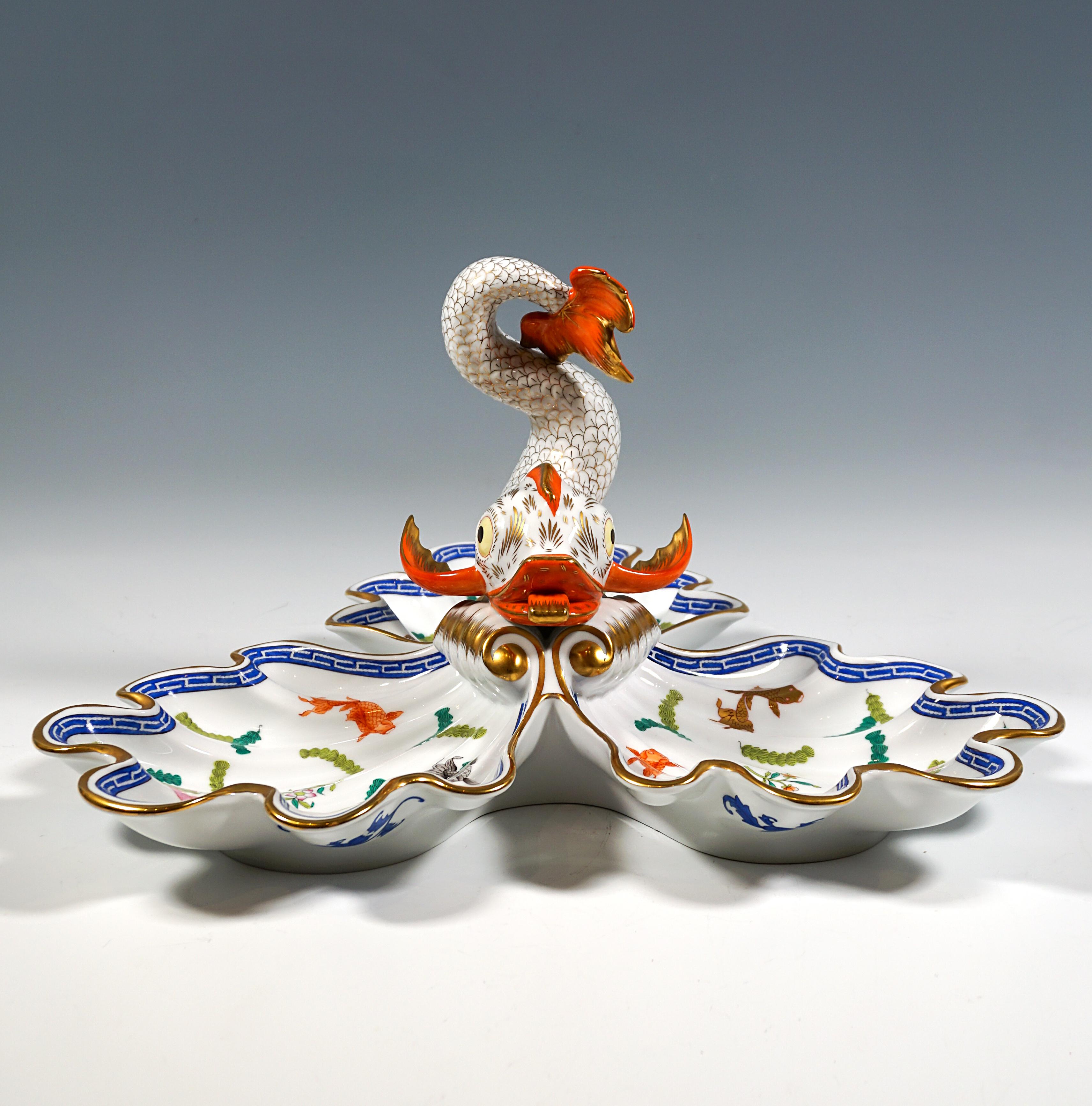 Large three-pass cabaret bowl in the shape of three open shell halves, volute-shaped waves crowned by a fully sculpted dolphin in the centre, richly decorated with aquatic plants and fish in vivid colours, blue meander border, gold highlights and