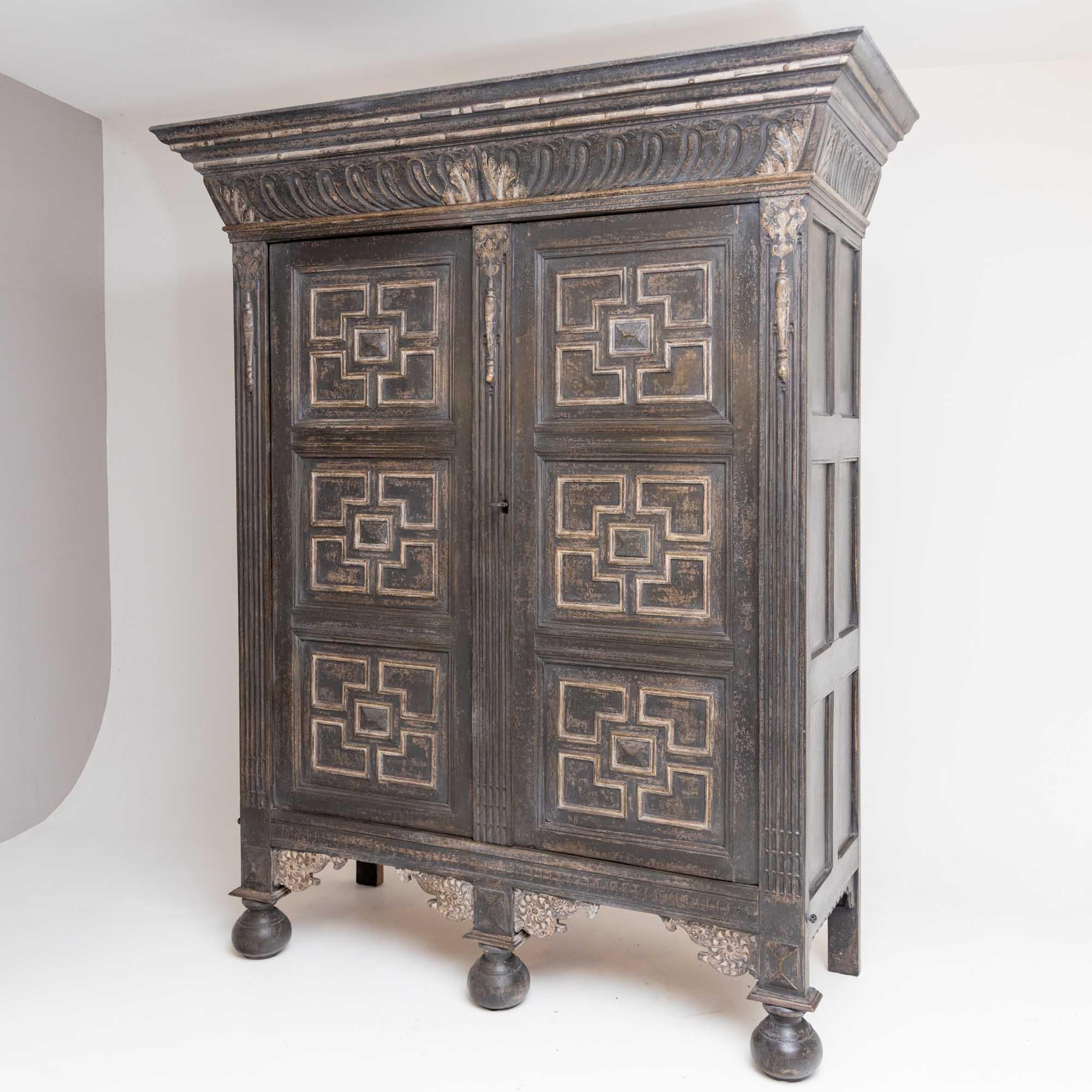 Large two-door cabinet on ball feet with a wide cornice and carved decorations. The doors have five-part panels and further carved decorations can be found in the corners between the feet. The anthracite-colored frame with white accents is new and