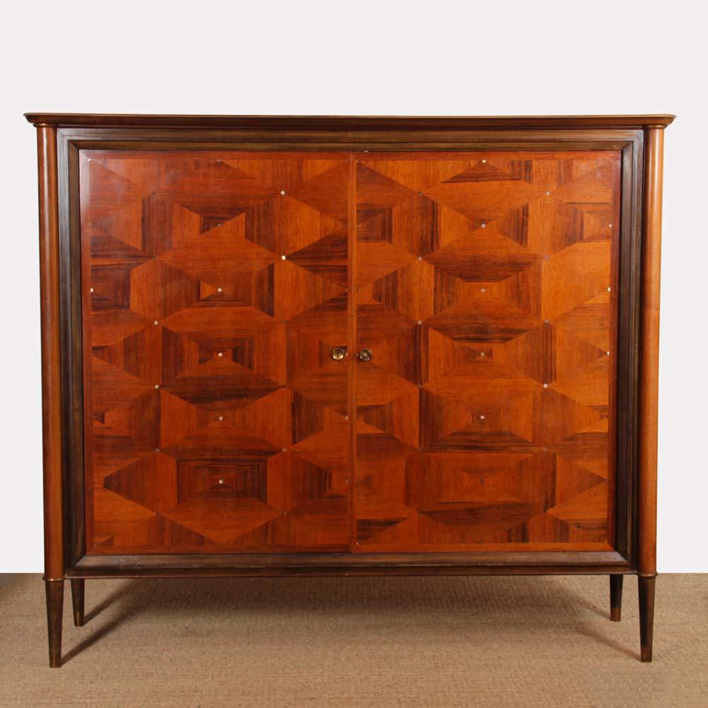 This large cabinet from the 1940s is made of mahogany and oak. It is decorated with mother-of-pearl pastilles and brass fillet at the top and bottom. It opens with two doors to shelves and two low drawers. It is in good original condition. It has