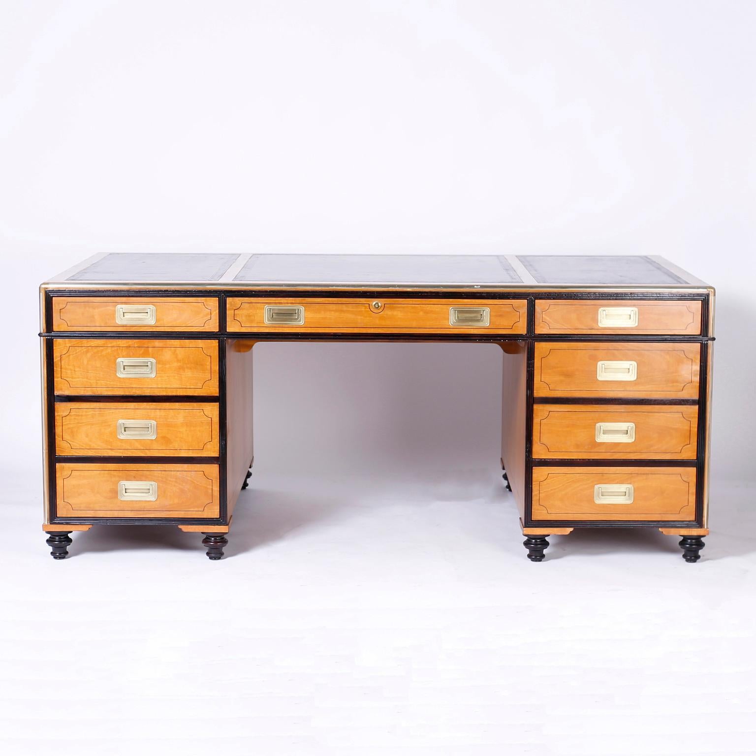 Midcentury partners desk crafted in satinwood with three tooled brown leather panels on top, Campaign style brass hardware, three drawers at the top of both sides with six additional drawers on one side and two doors on the other, ebonized borders