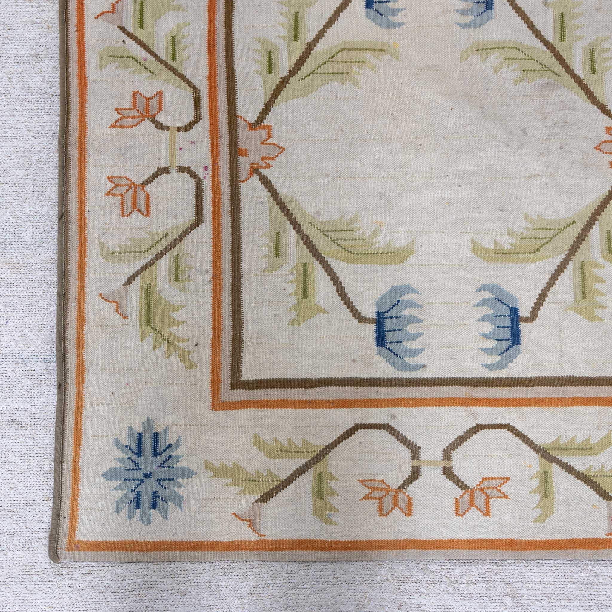 Large 1970s carpet with floral decoration on beige ground and surrounding framing in orange and brown. Signs of age and use.