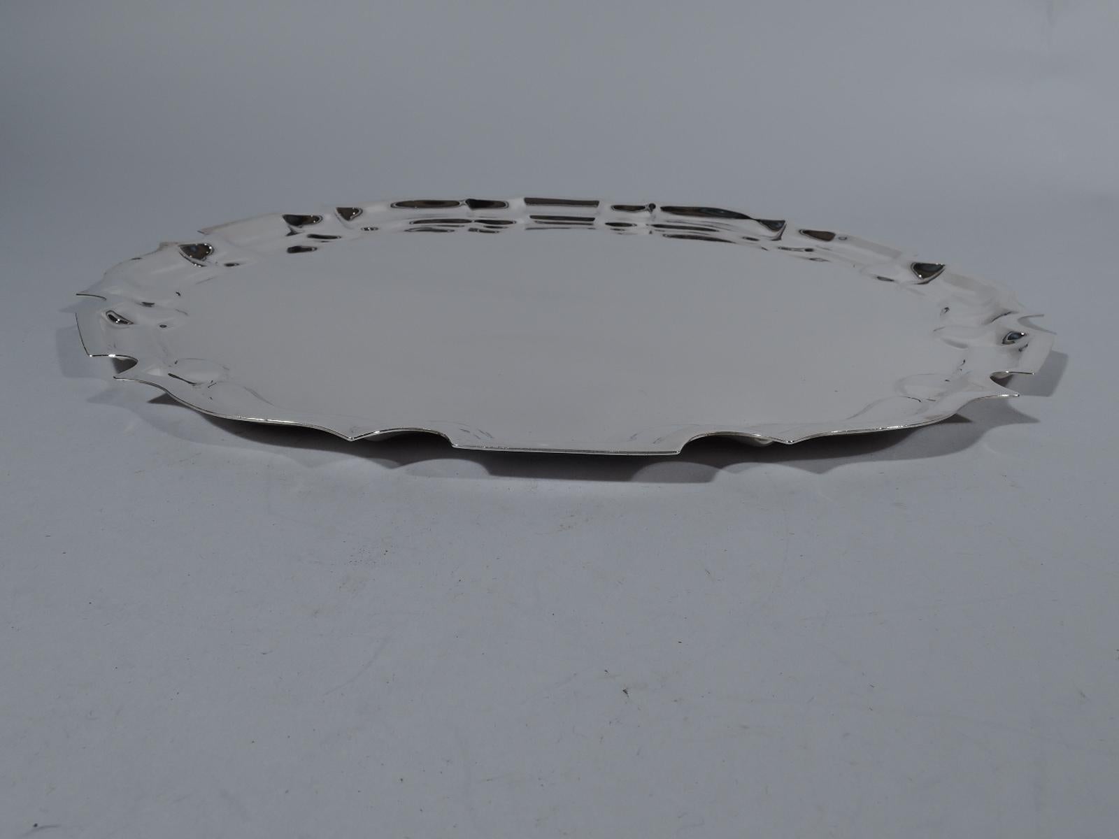 Traditional sterling silver serving tray, circa 1950. Retailed by Cartier in New York. Round with flat curvilinear Georgian piecrust rim. Fully marked including maker’s (Graff, Washbourne & Dunn) and retailer’s stamps and no. 64. Weight: 31 troy