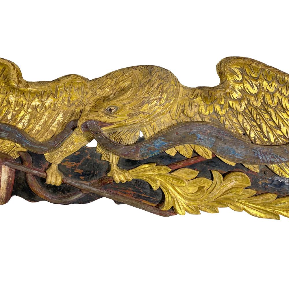 Carved from pine, the gilded eagle with its head turned right grasping a painted blue ribbon in its mouth. One talon holds an American flagstaff while the other talon holds a gilded olive branch. Attributed to Boston Artistic Company, circa