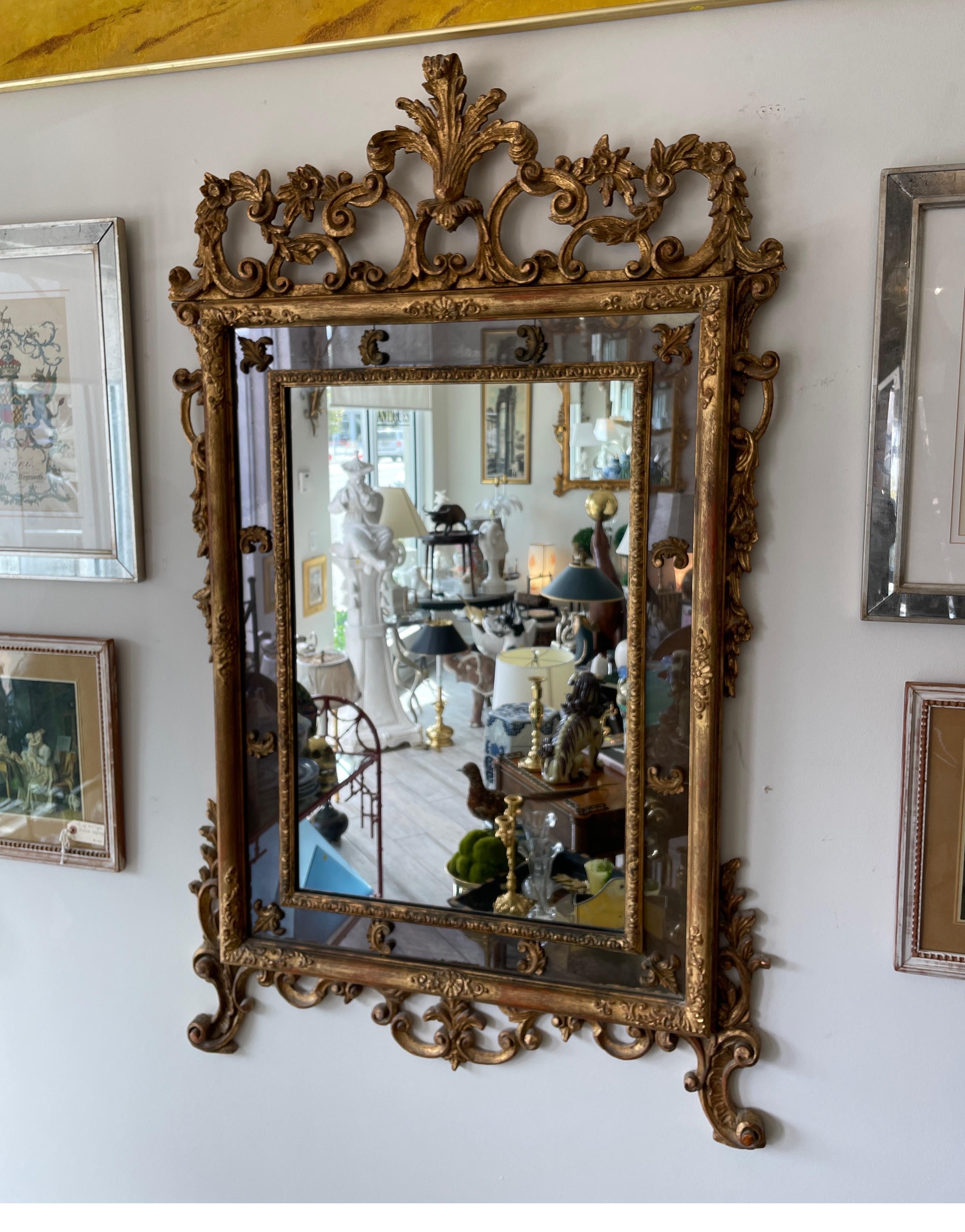 Exceptional carved and gilded Italian mirror. Center clear mirror plate with a surround of smoked mirror adorned with carved fleur de Lys pieces. The entire outside of mirror is adorned with carvings & topped with a large plume.